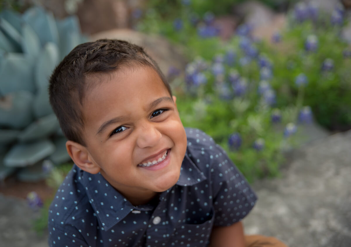 A little boy smiling with flowers in the background