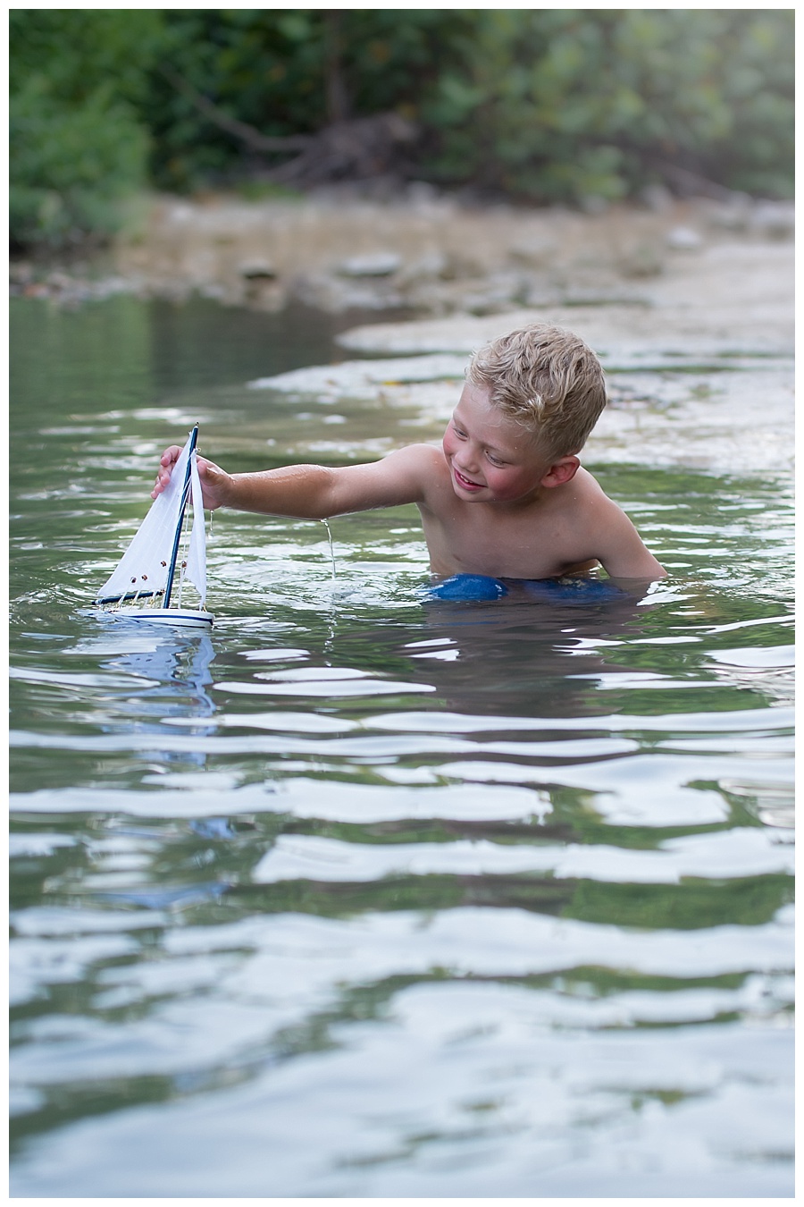 blonde toddler playing with a sailboat in a creek