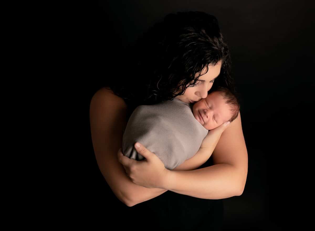 Mom kissing her new baby boy while the baby is smiling.