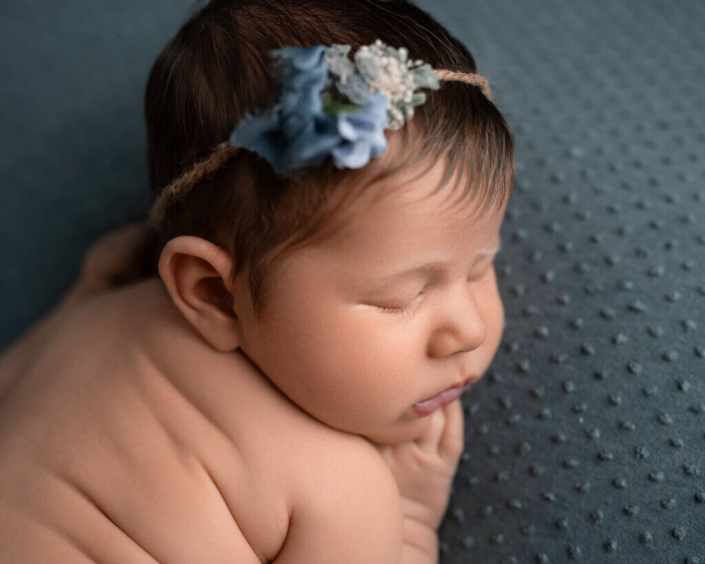 Sleeping newborn girl wearing a blue floral headband on a teal textured blanket