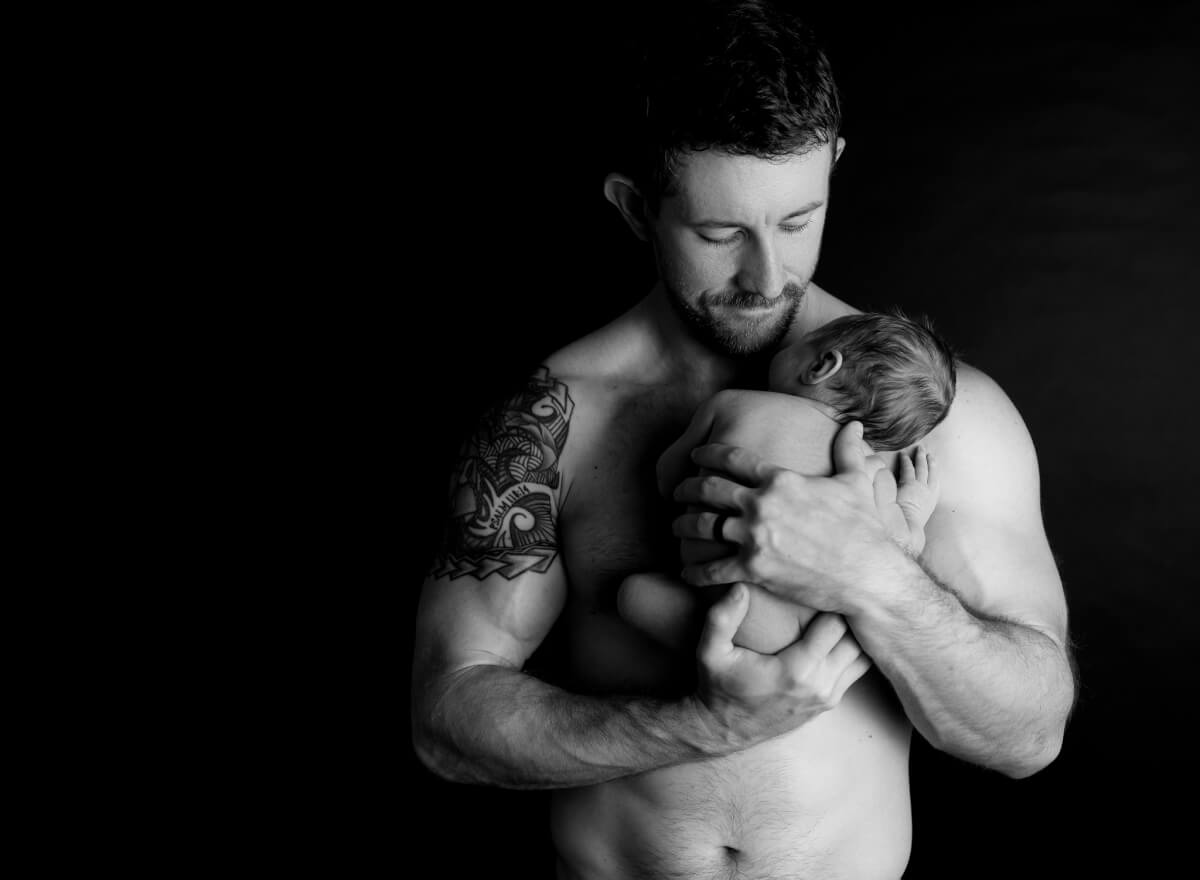 Dad holding his sleeping newborn against a dark backdrop in a Leander studio