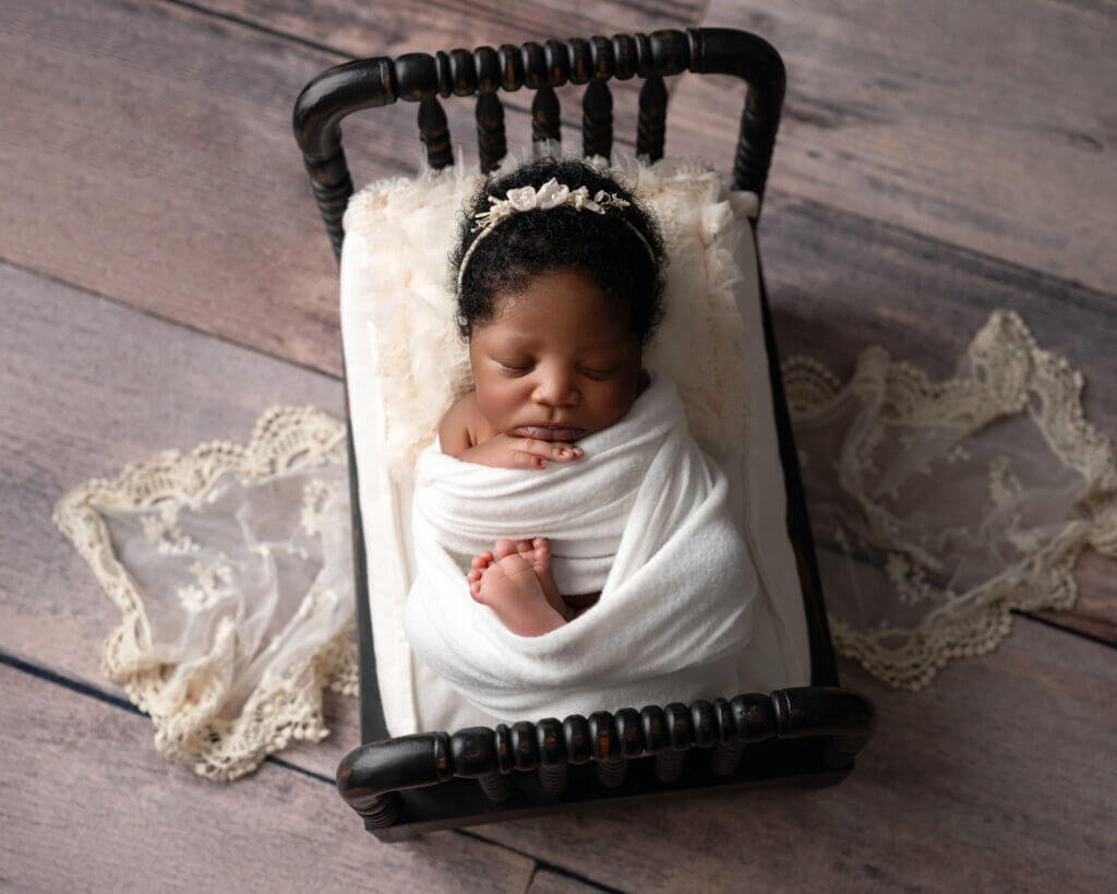 angelic baby wrapped in white sleeping on black wooden tiny bed for newborn photos in austin