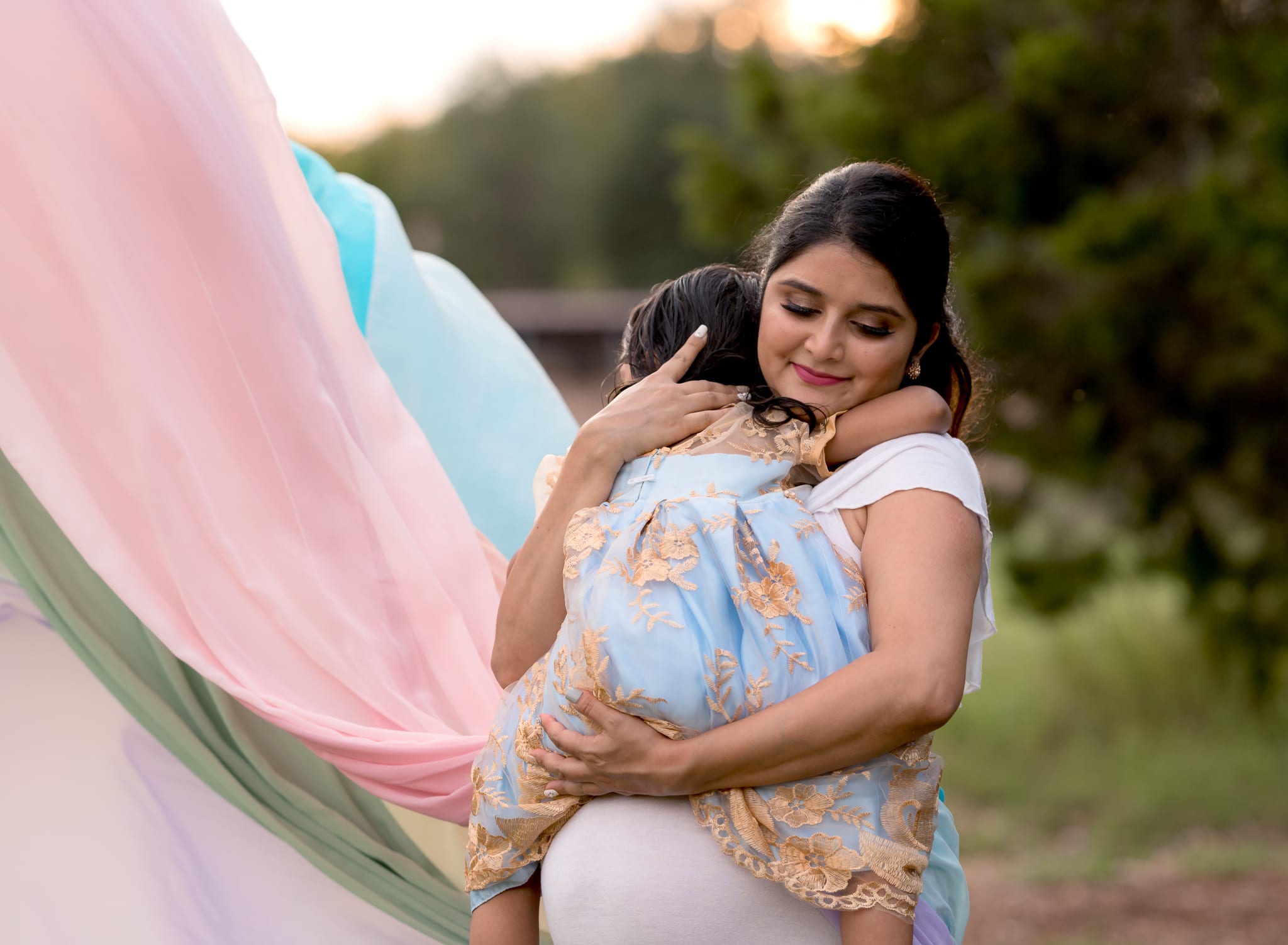 Pregnant mom in a rainbow dress holding her oldest daughter.