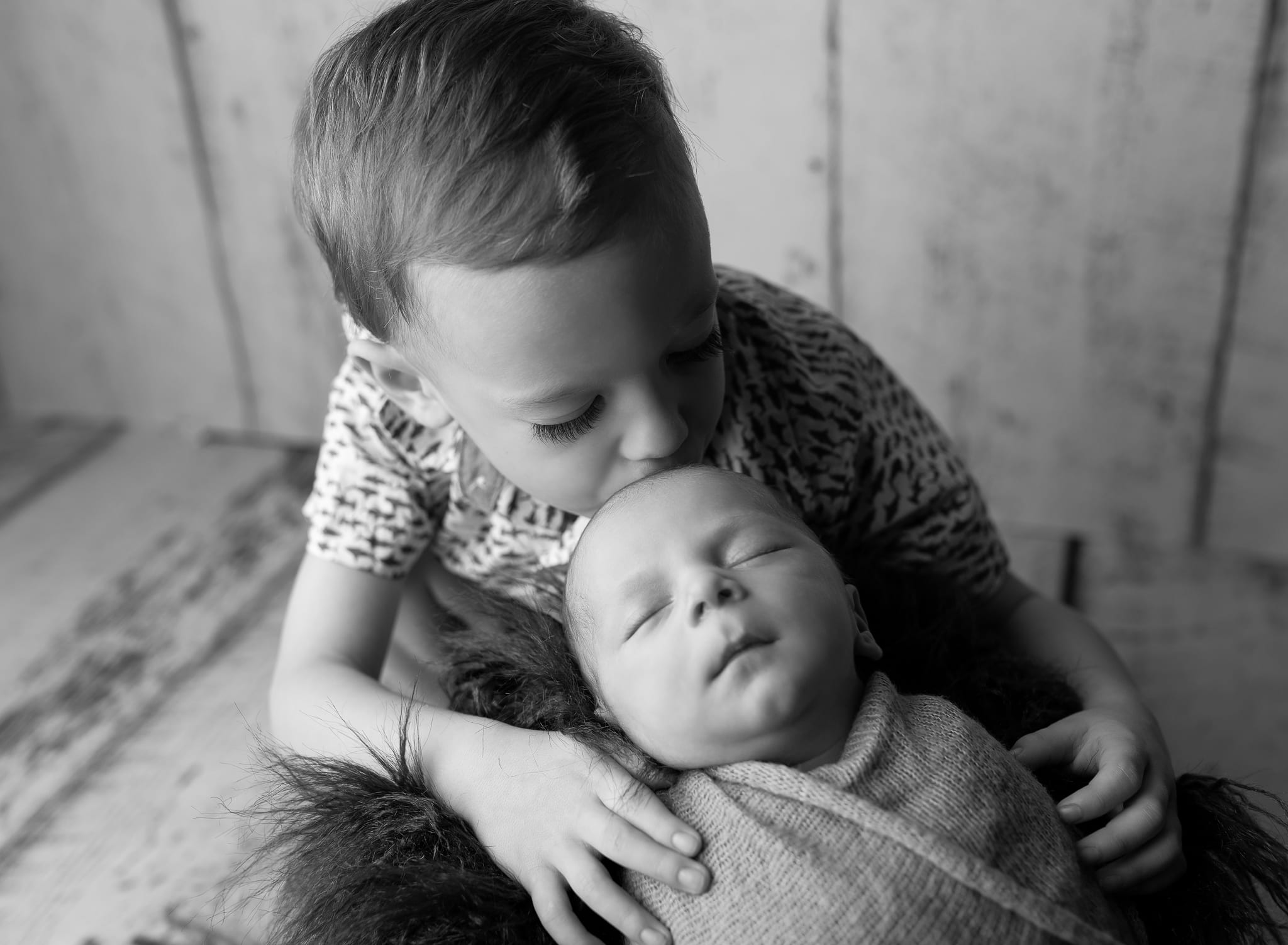 older boy kissing his new baby brother on the head
