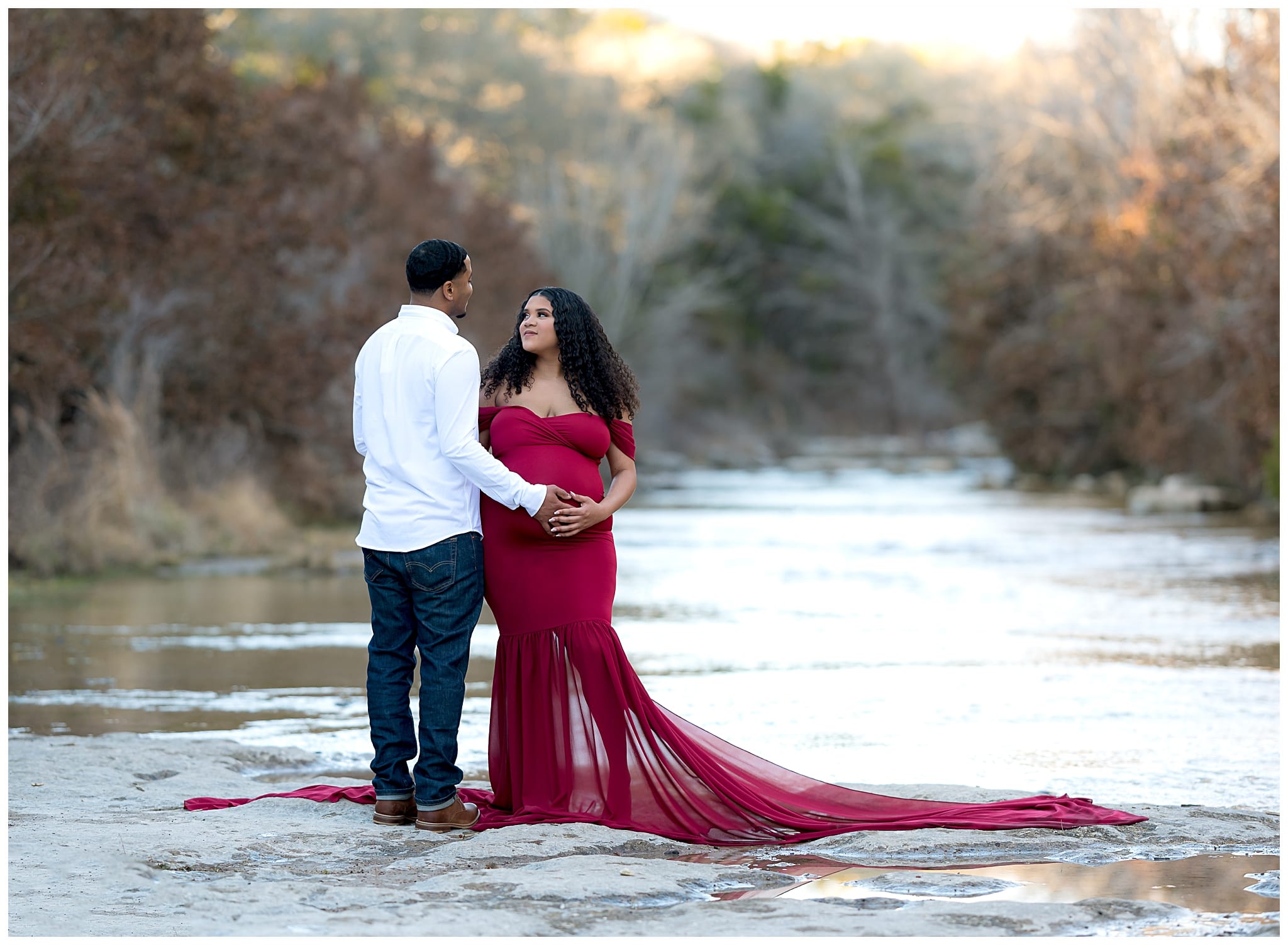 couples maternity portrait by a creek with red dress.