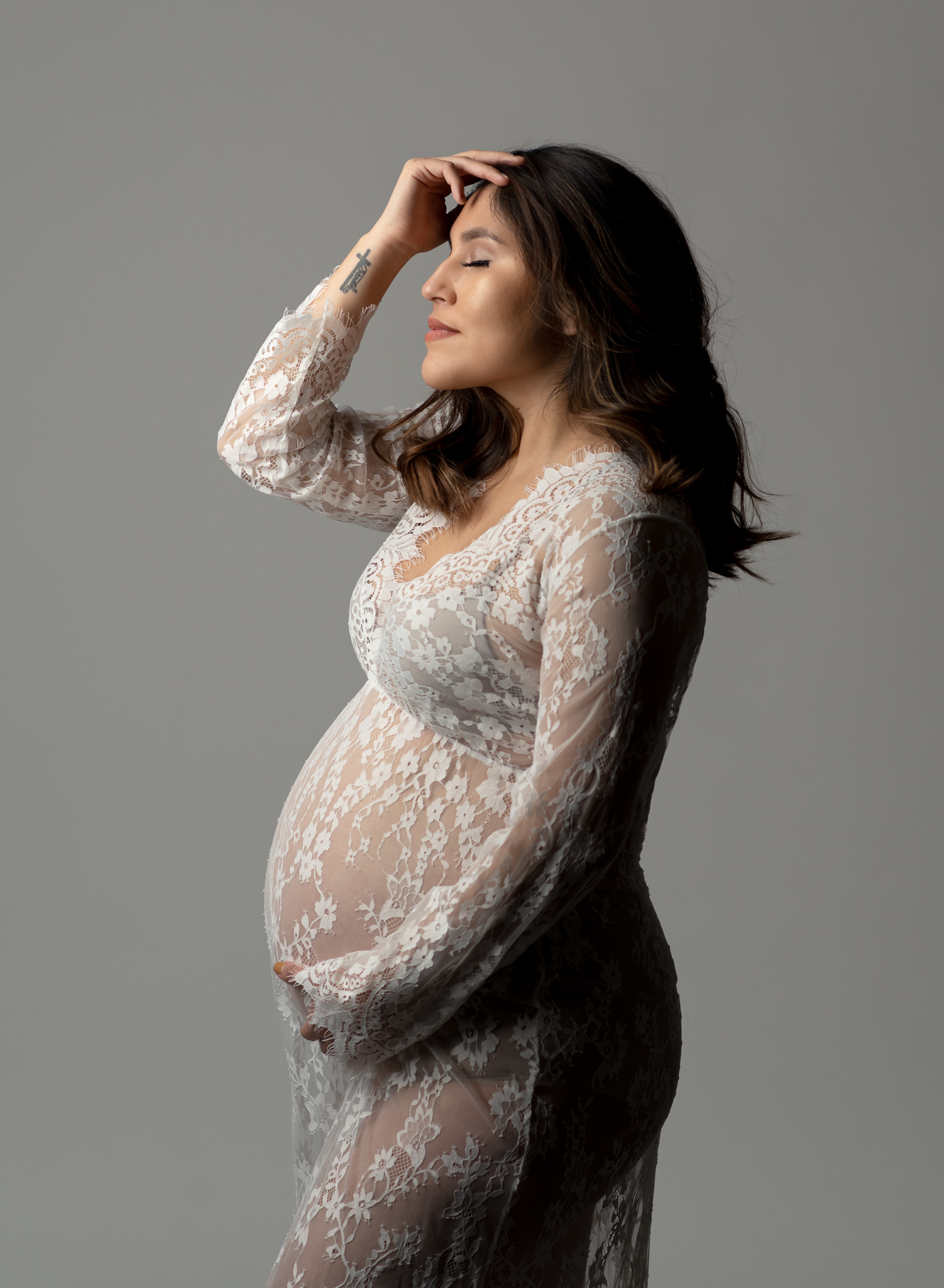 studio maternity portrait of woman in white lace dress