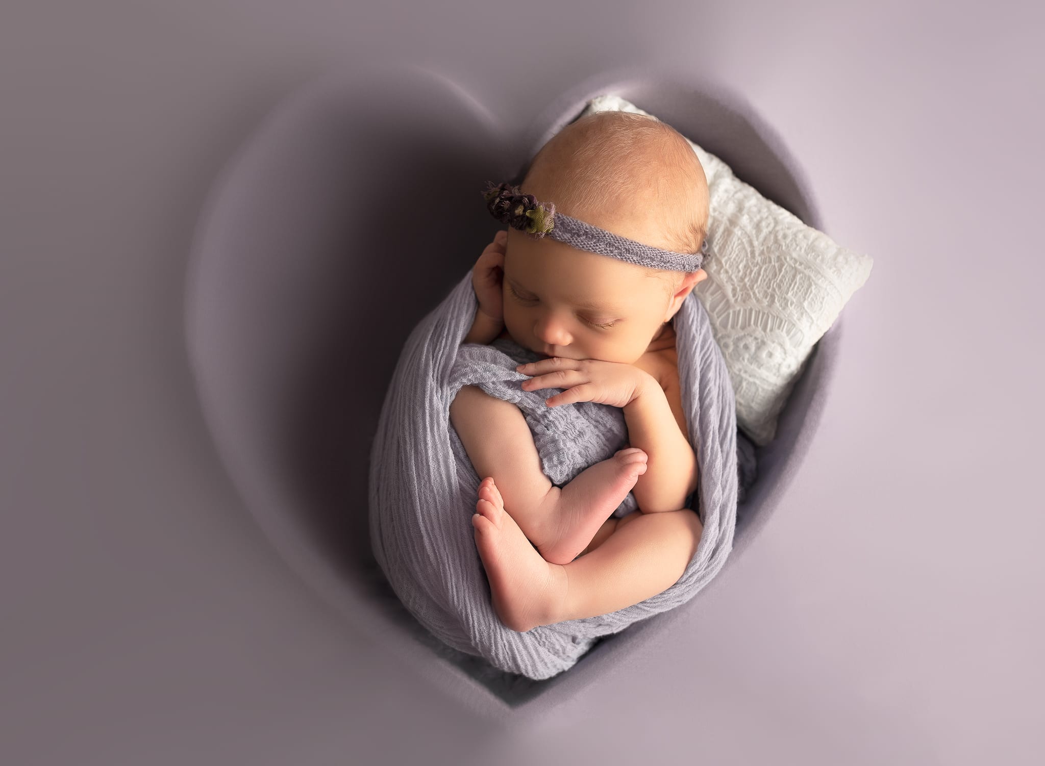 newborn baby in a heart bowl on purple