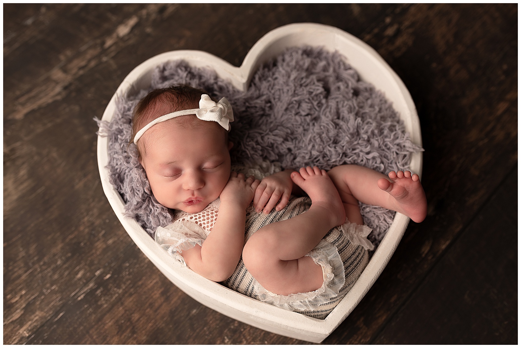 newborn baby sleeping in a white wooden heart bowl