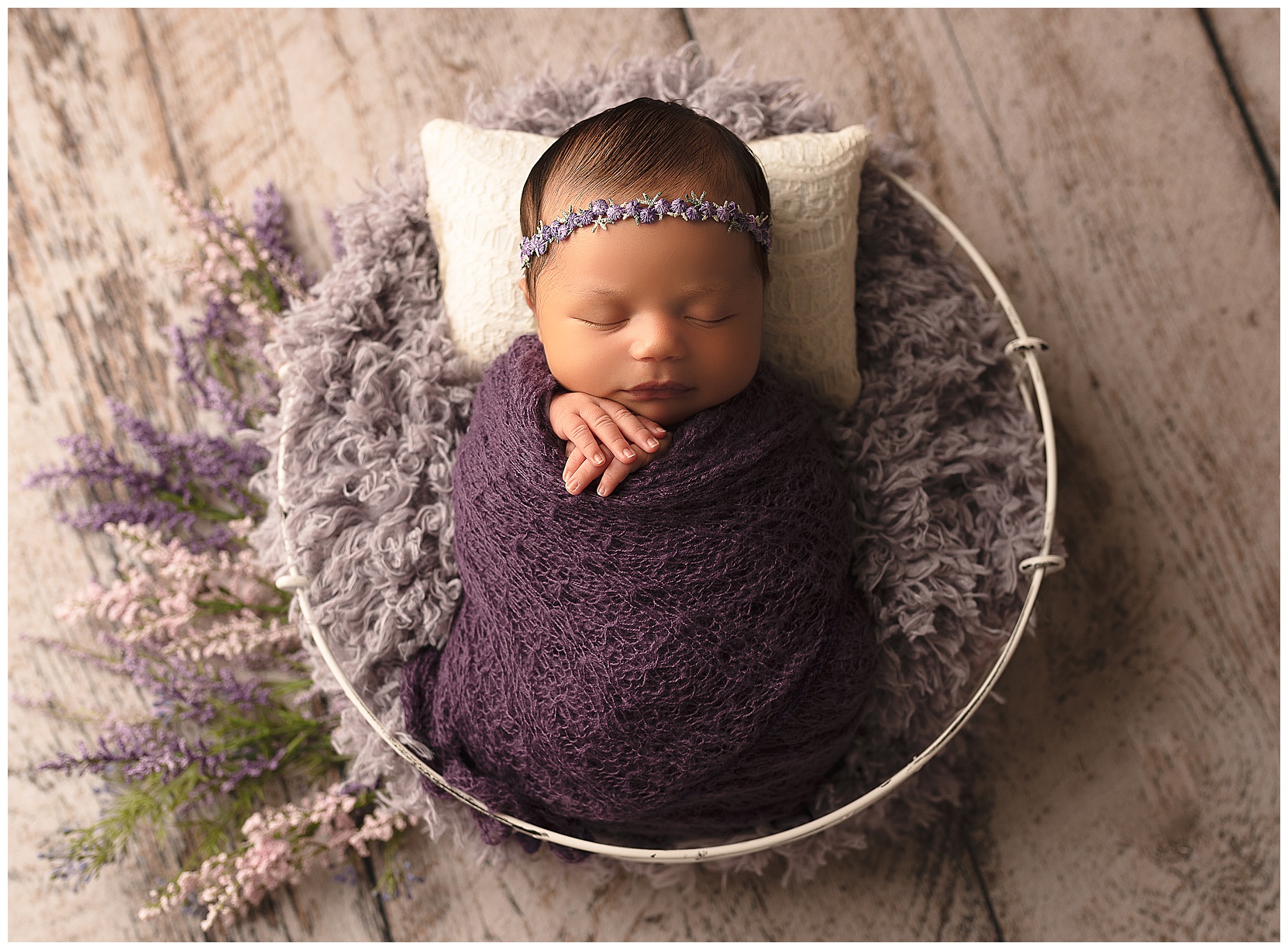 newborn baby girl with a purple wrap and purple headband in a white bowl