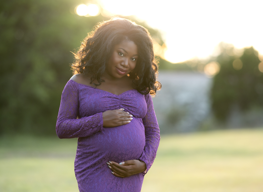A pregnant woman wearing a purple lace dress at sunset.