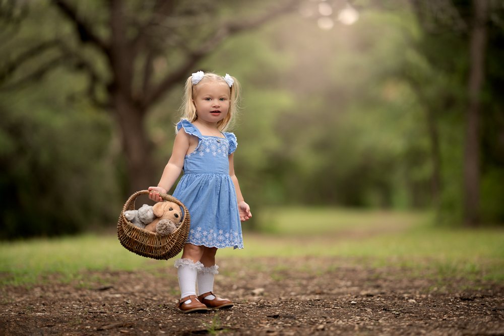 little girl in a blue dress carrying a basket of her favorite stuffed animals