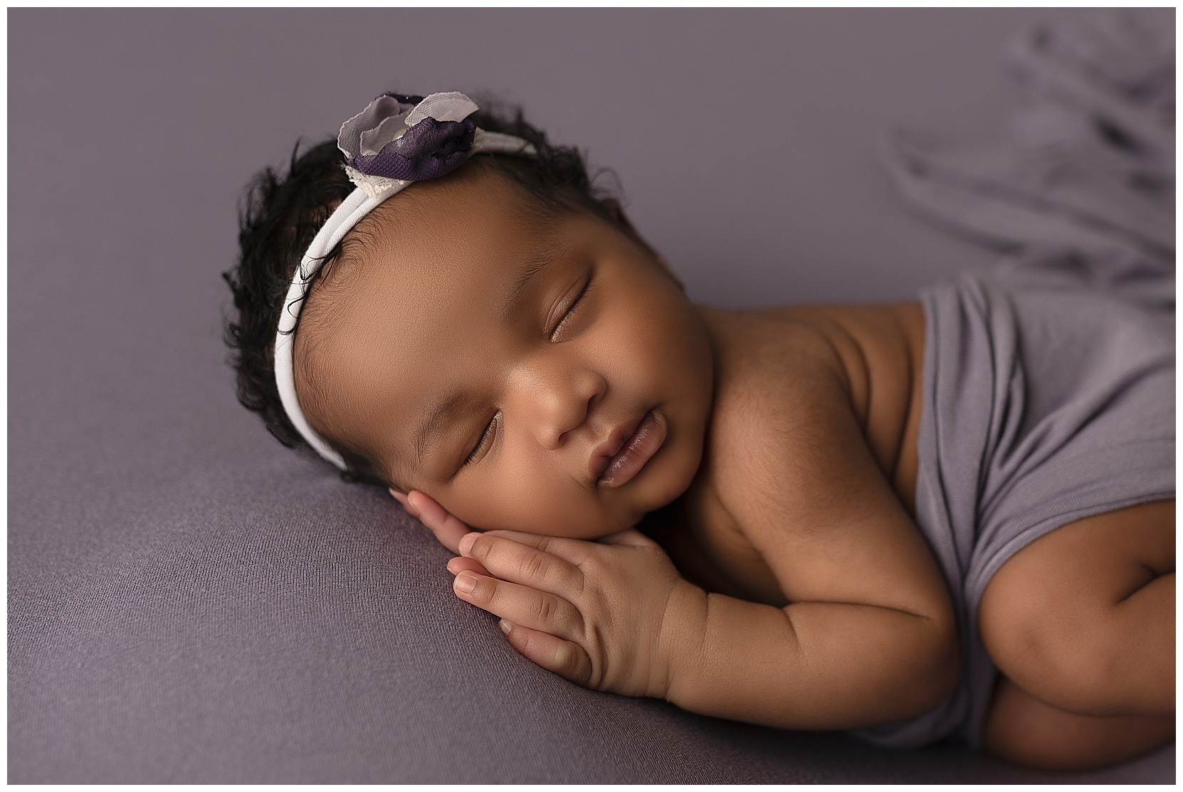 sleeping baby laying on her side on a purple fabric