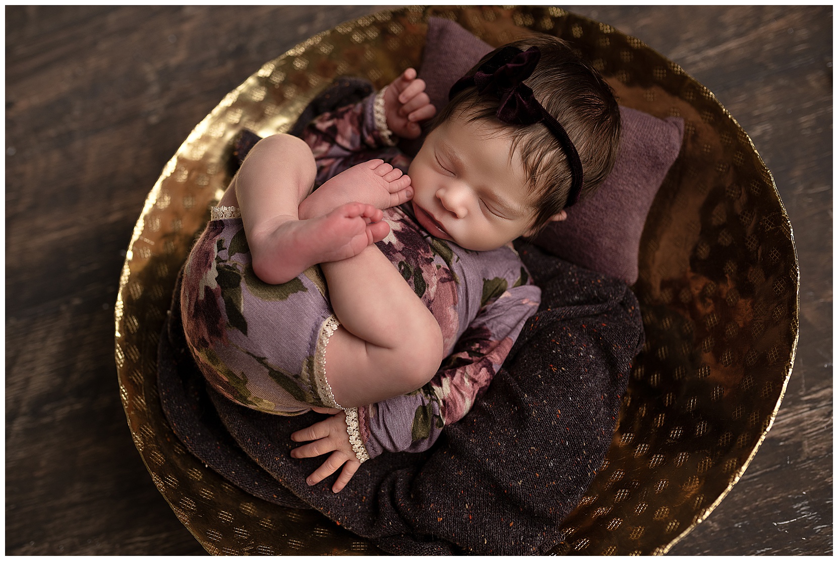 baby girl sleeping in a gold bowl wearing a purple floral romper