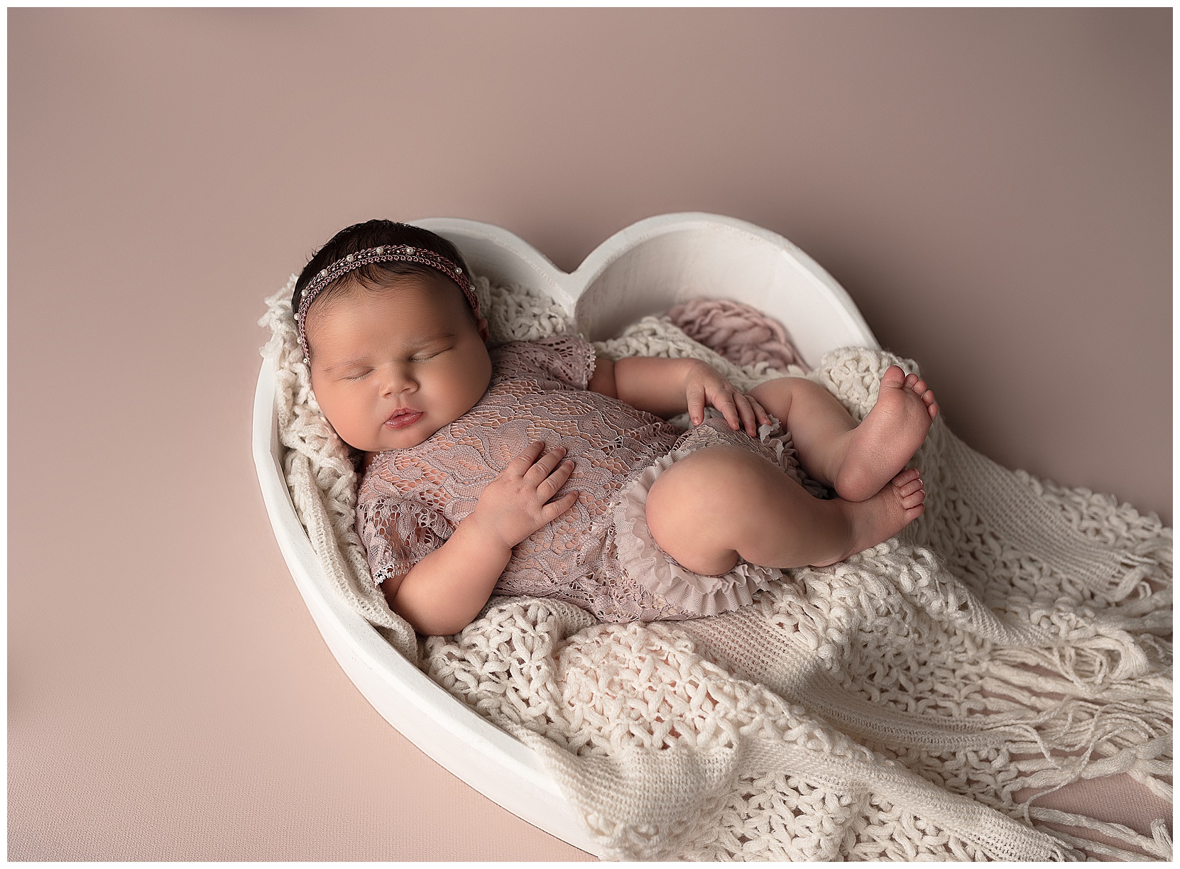 sleeping baby girl wearing a lace romper sleeping in a white heart shaped bowl