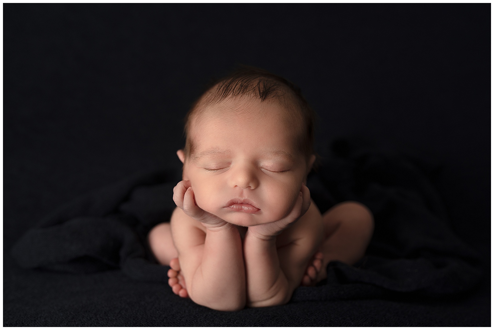 baby sleeping in the froggy pose on a dark blue blanket