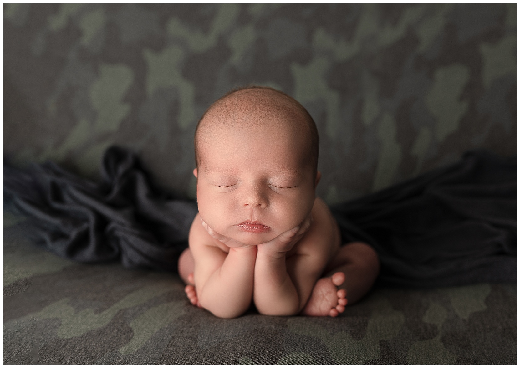 baby sleeping in the froggy pose on a green camo blanket