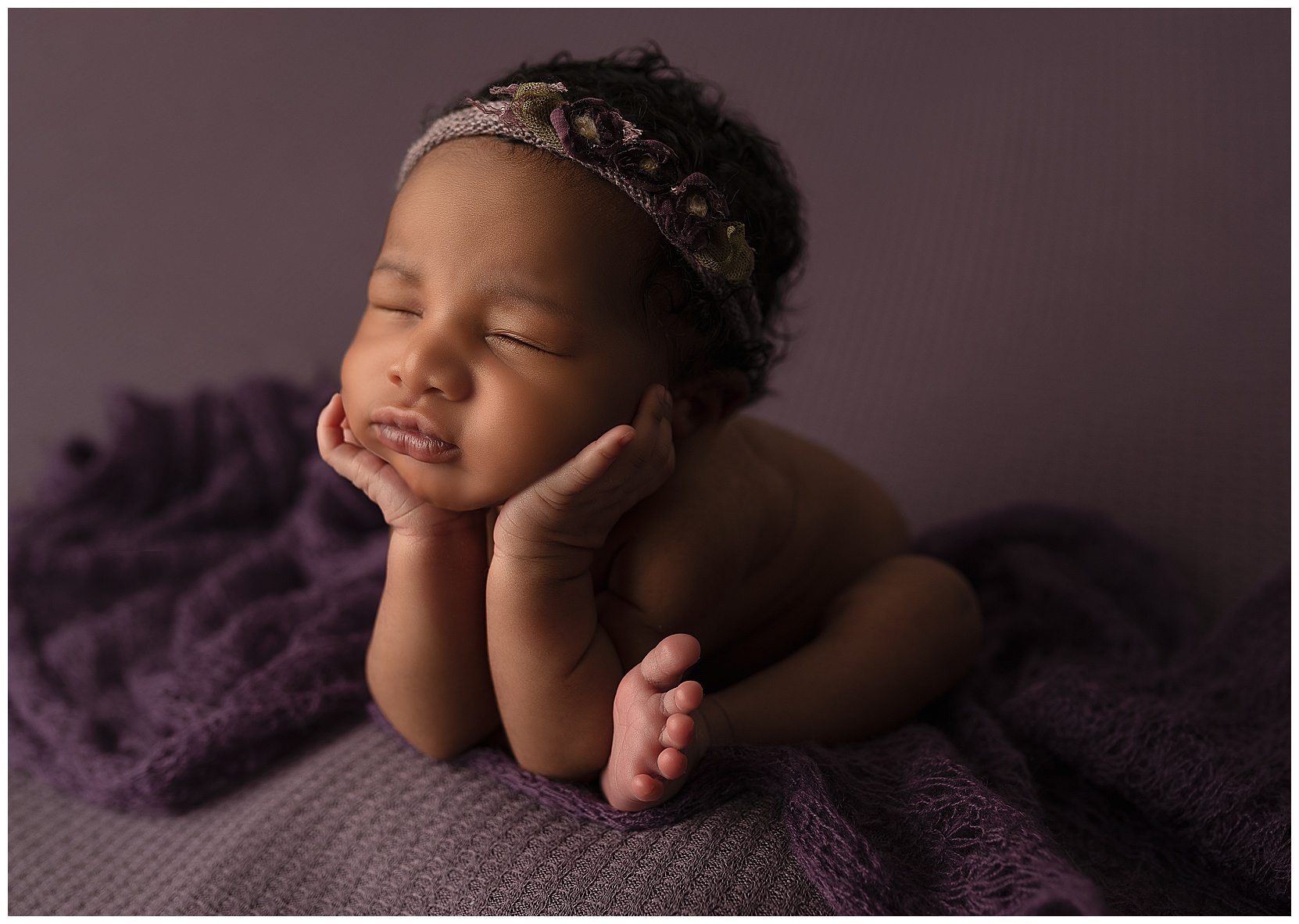 side photo of a newborn baby sleeping in the froggy pose on a purple blanket