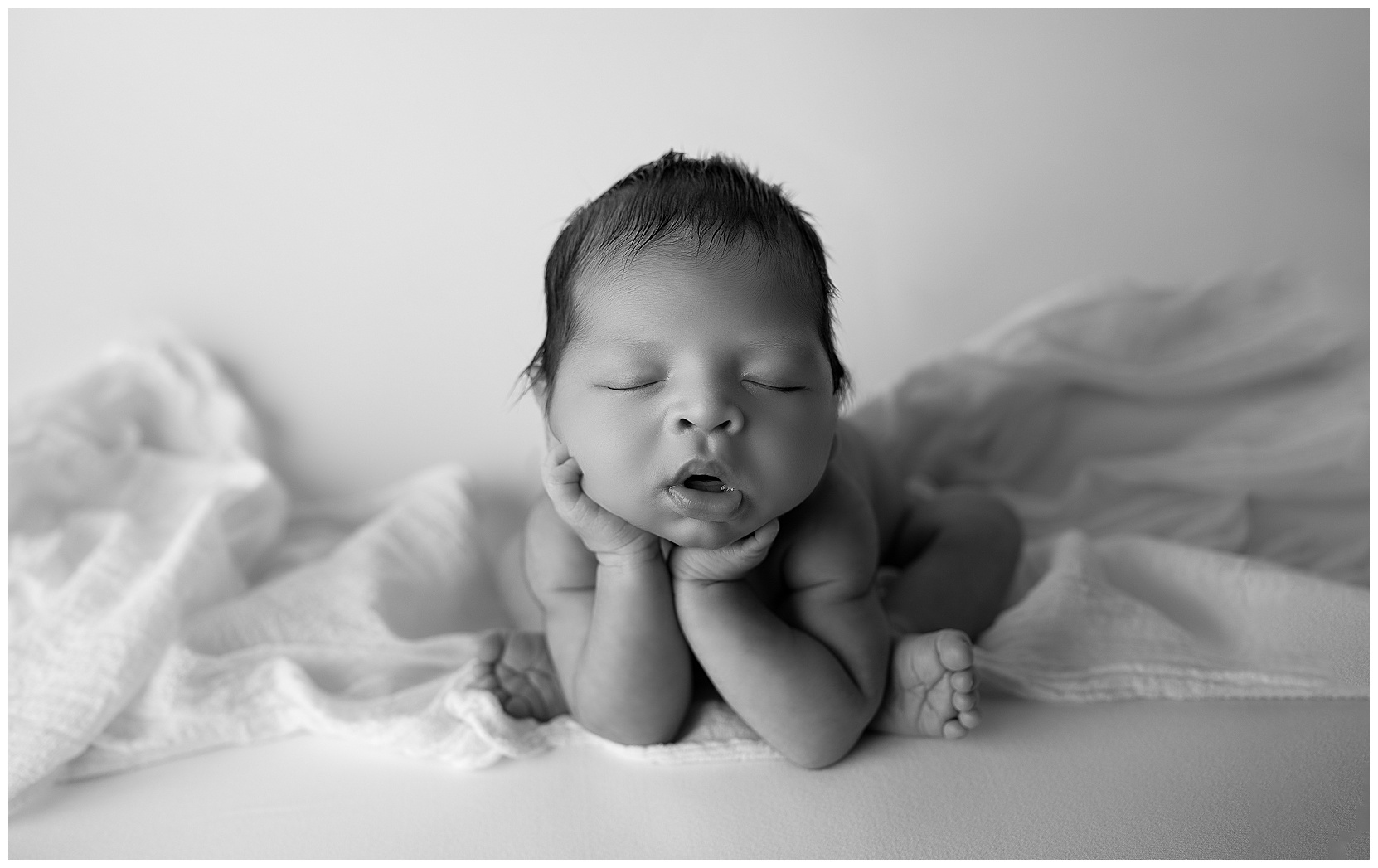 newborn baby in the froggy pose in a black/white photograph