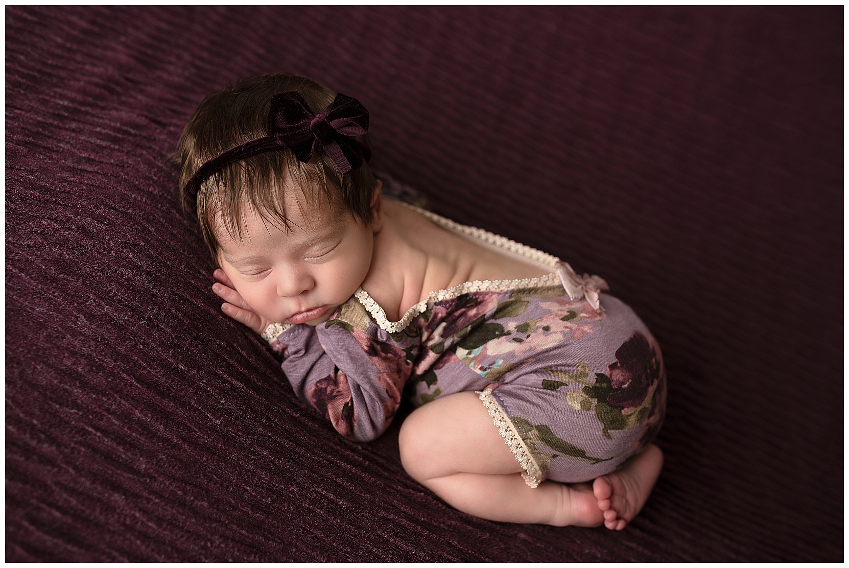 baby girl sleeping on a purple blanket wearing a purple floral romper