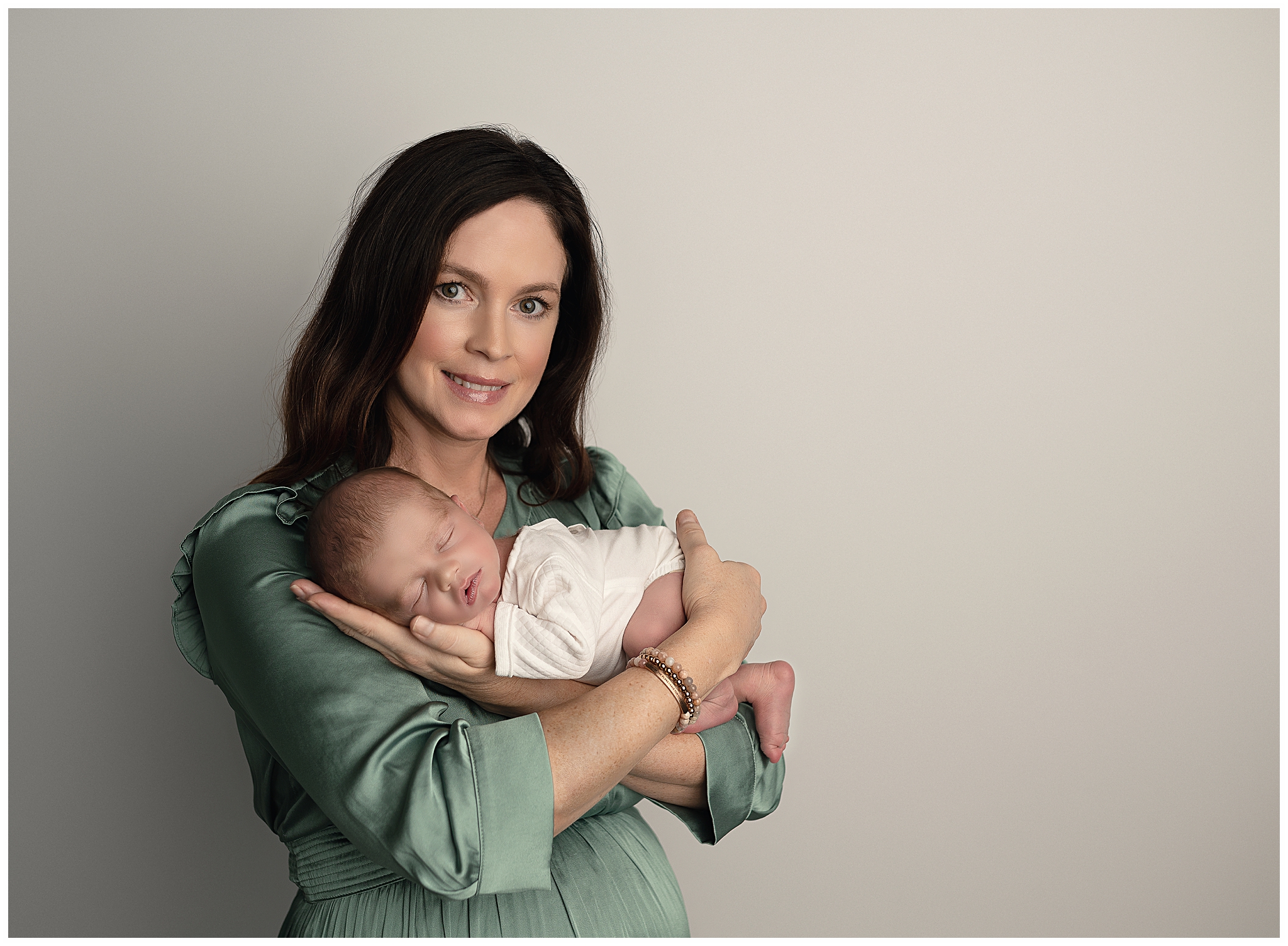 mom green dress holding new baby white outfit