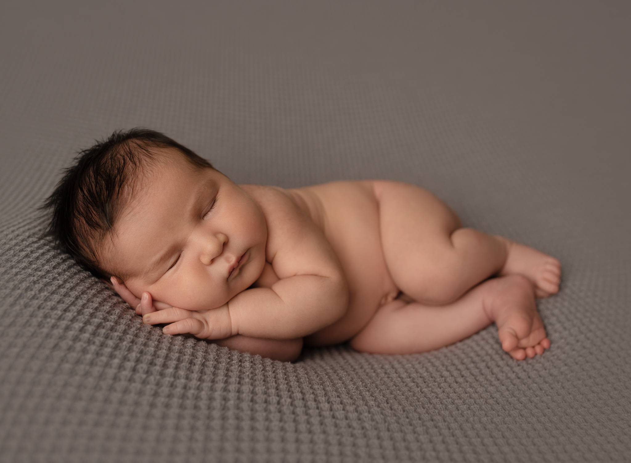 newborn baby boy sleeping on a gray waffle blanket