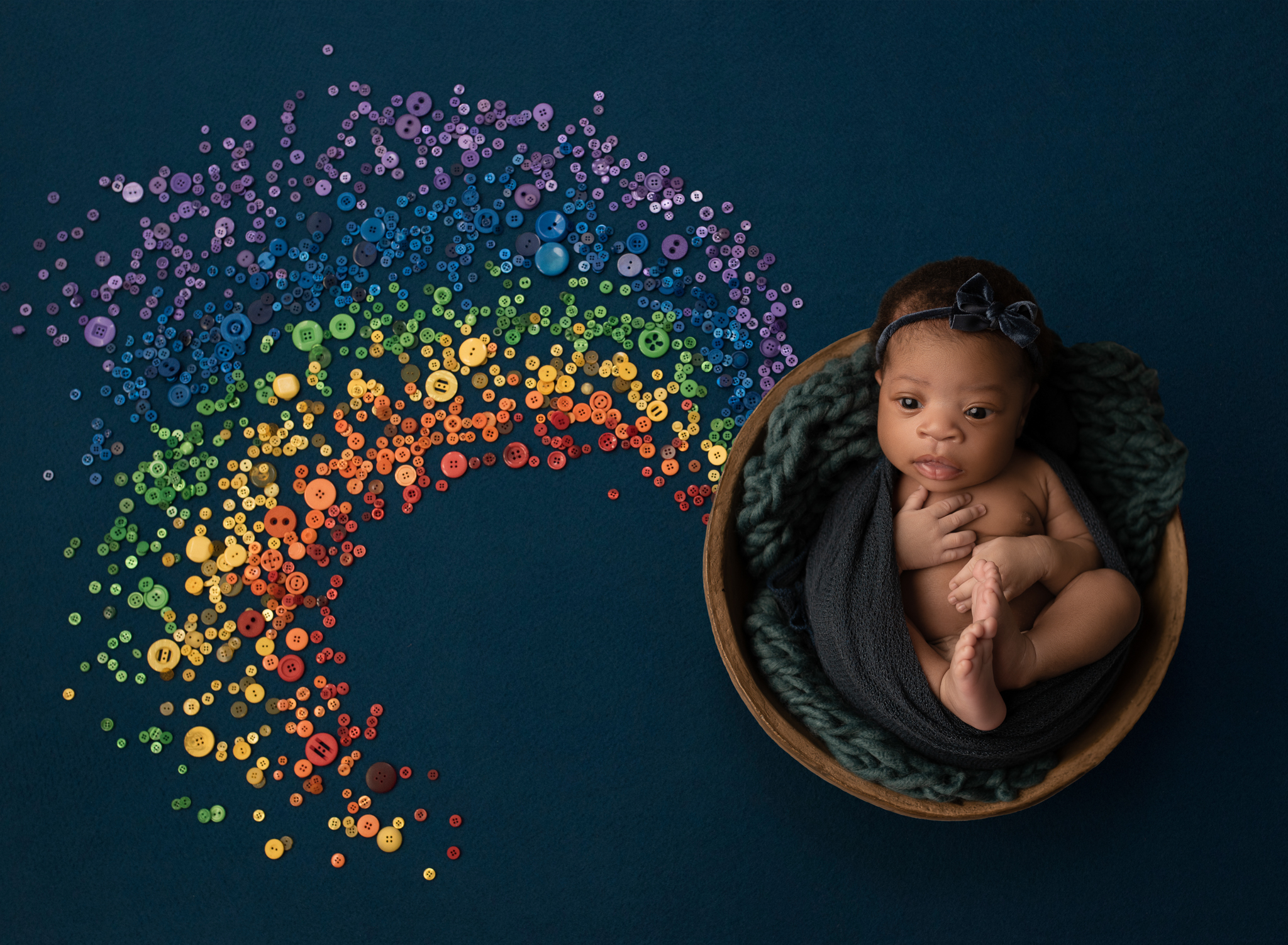 baby laying in a bowl at the end of a rainbow made of buttons