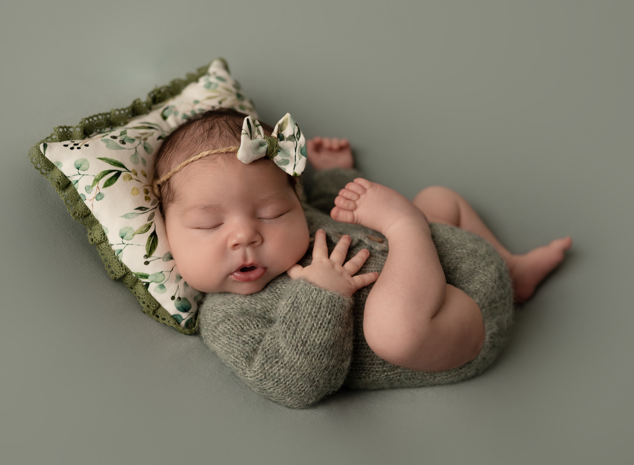 sleeping baby girl green knit romper green backdrop floral pillow