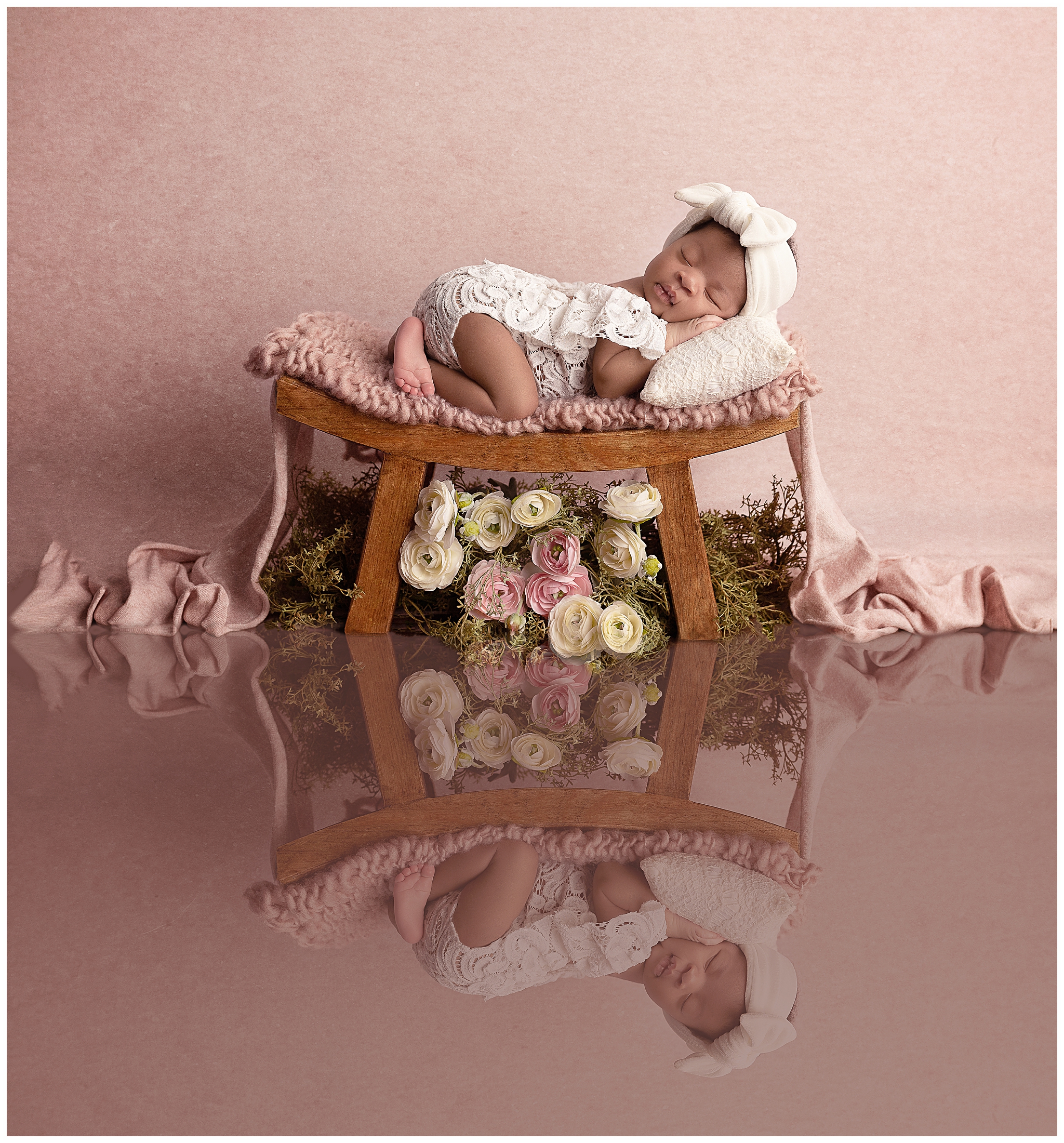 African American sleeping newborn in white lace posed on a bed over flowers and a pink backgound