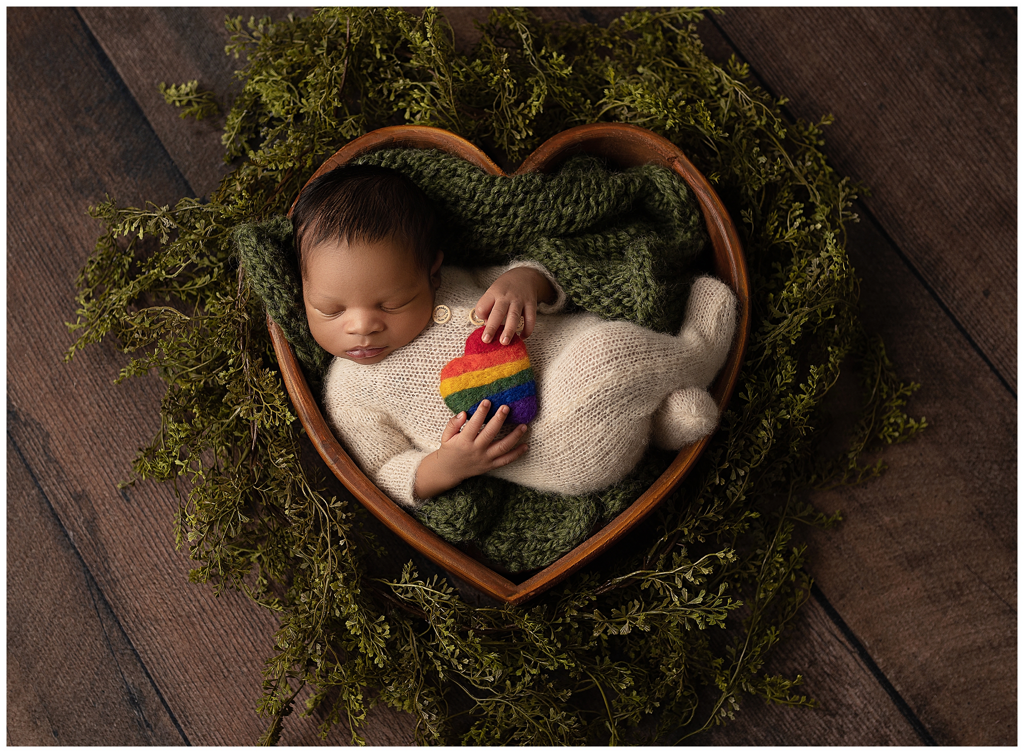 baby sleeping in a brown heart bowl surrounded by greenery