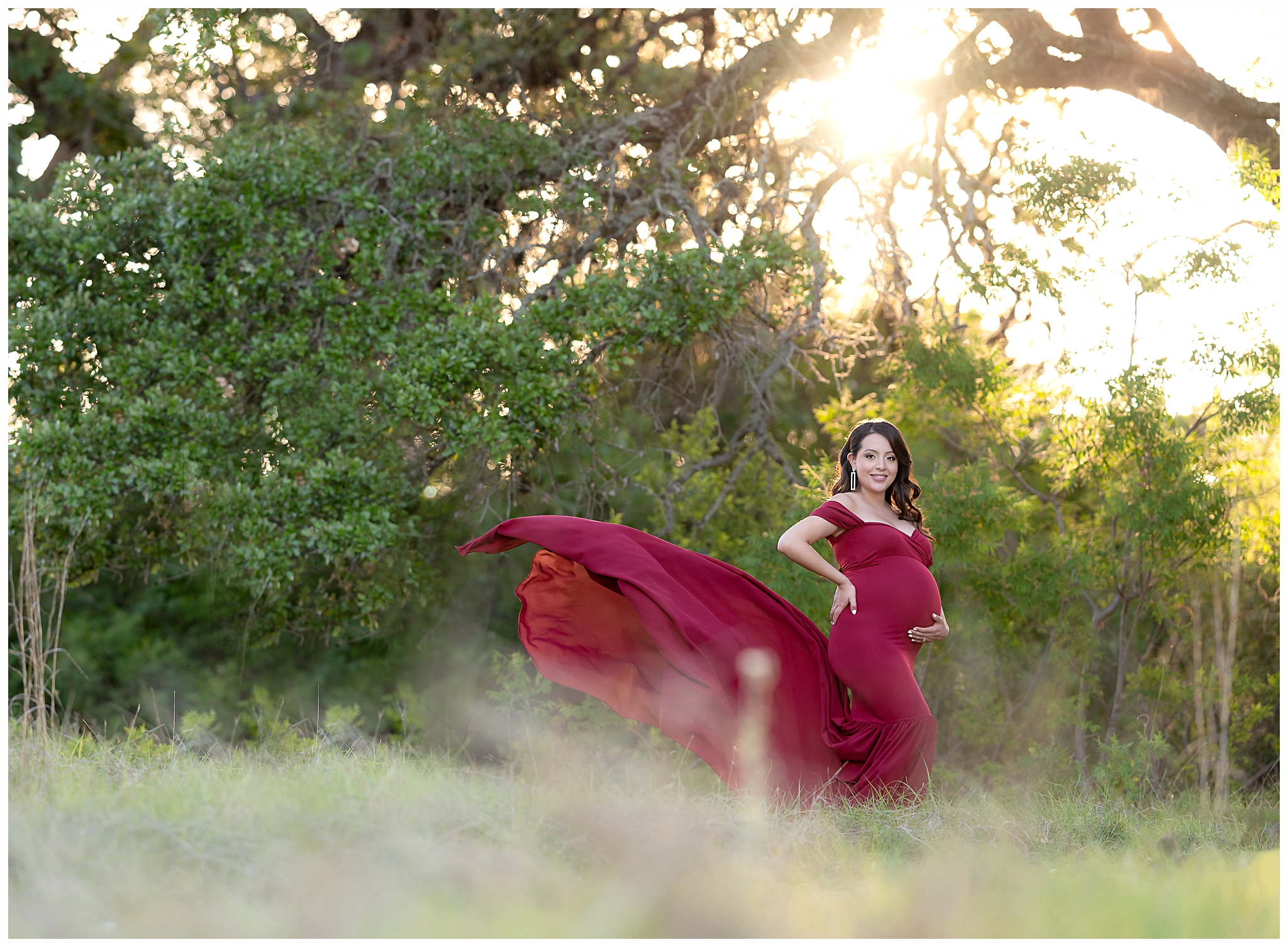 Pregnant woman in flowing maternity gown in front of scrub brush and a sunset