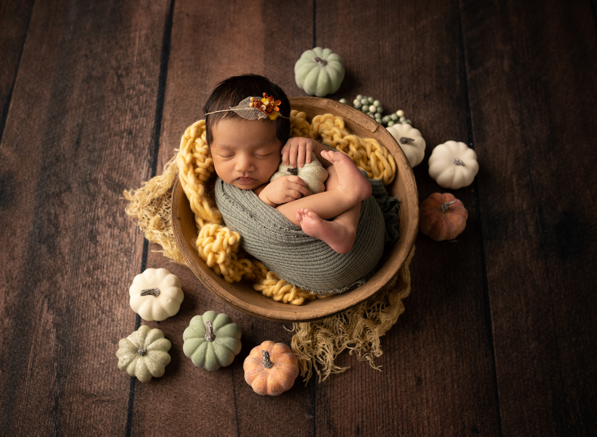 baby girl sleeping in a bowl surrounded by mini pumpkins