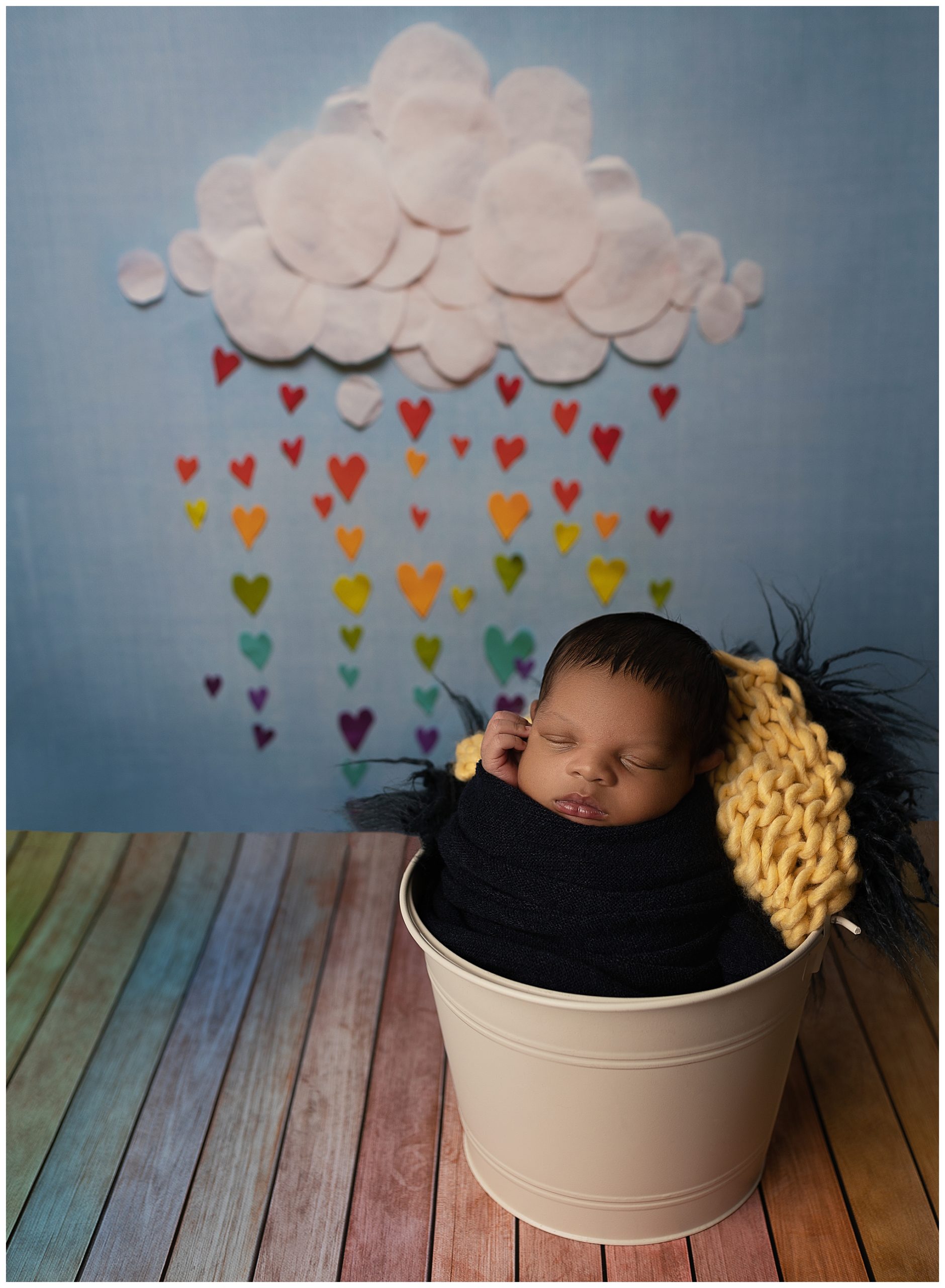 newborn baby in a bucket with a Rainbow baby photography themed background