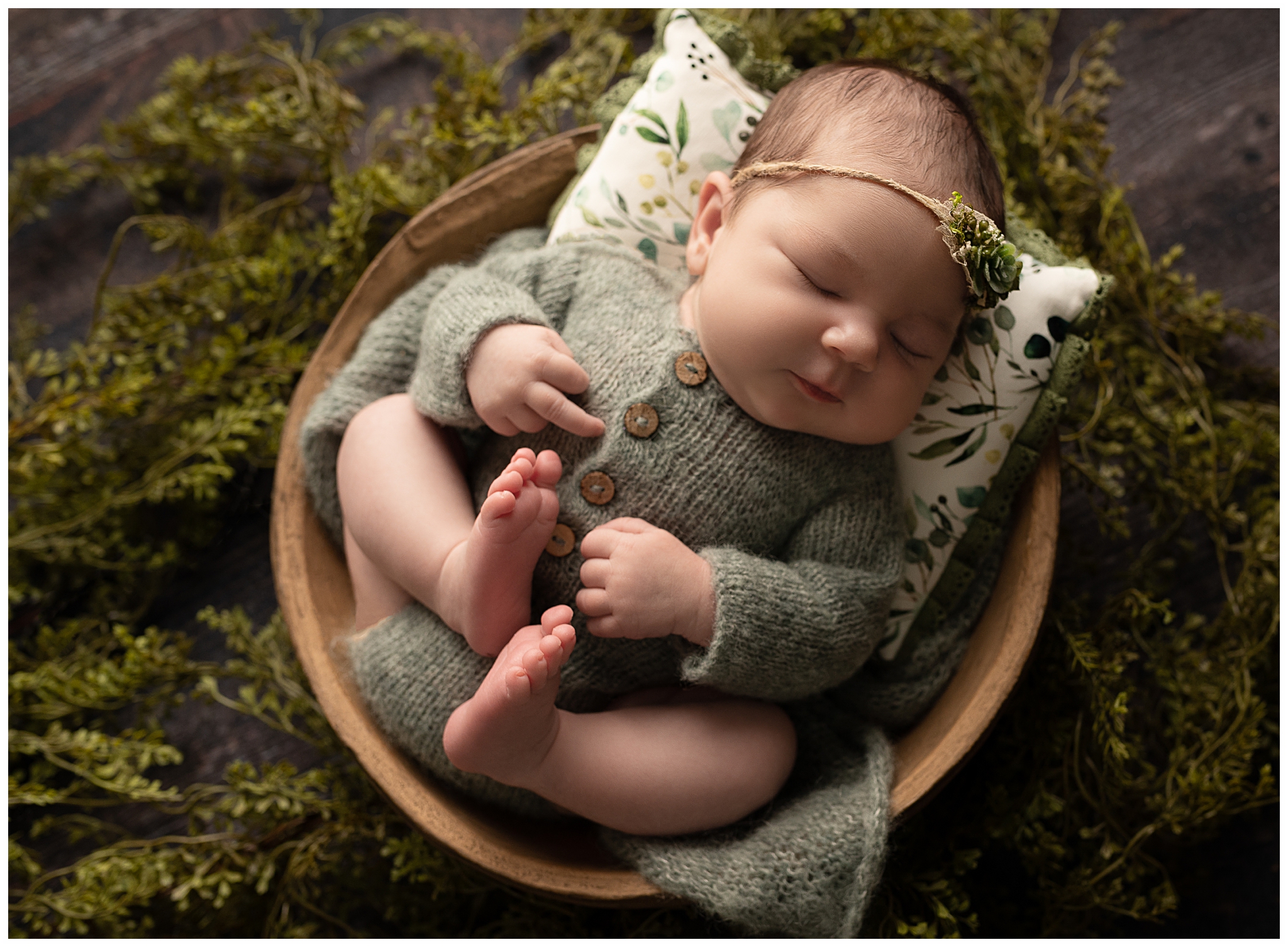 Baby giving the middle finger while sleeping in a brown bowl surrounded by greenery