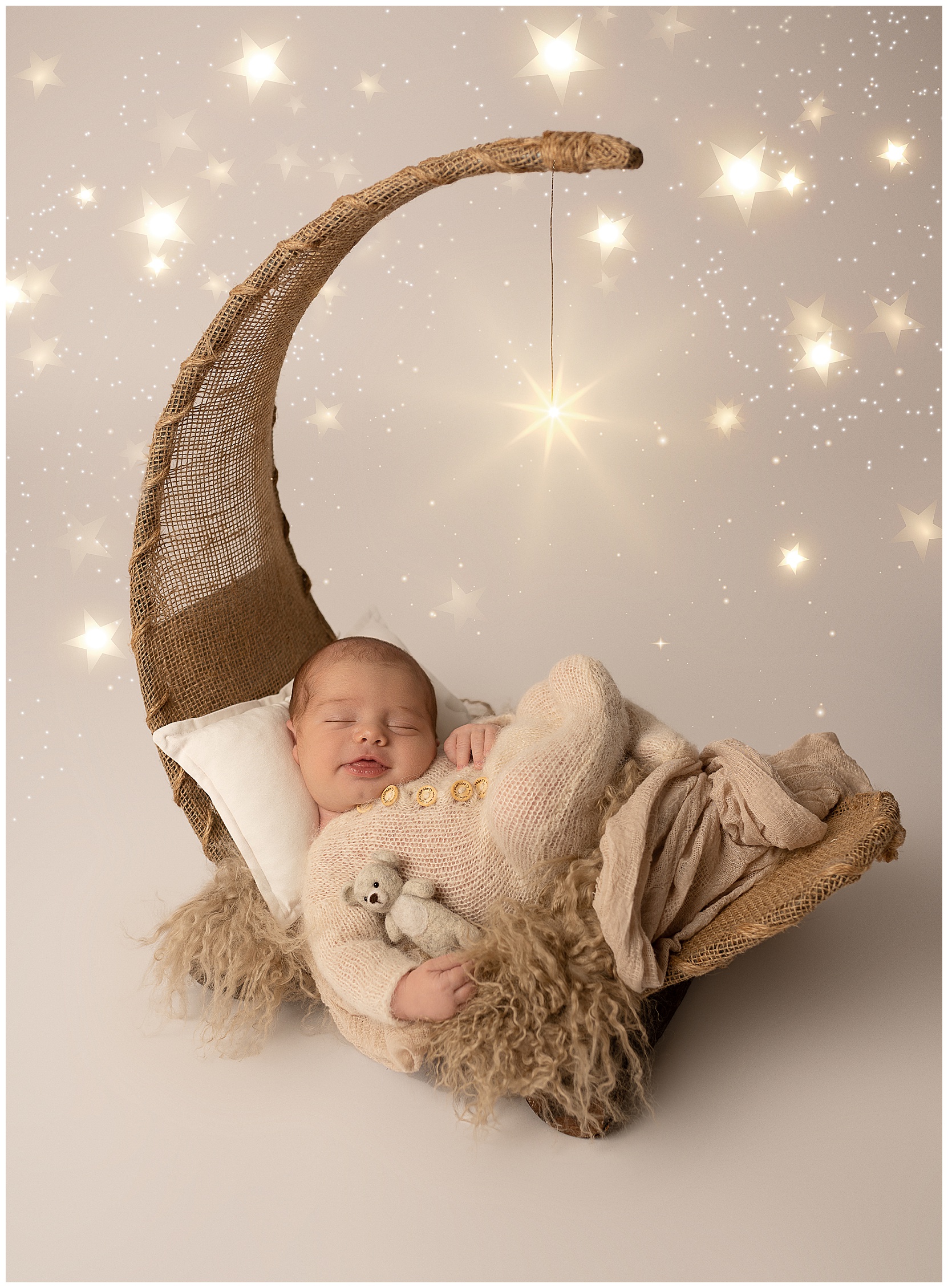 High end newborn photography featuring a smiling, sleepy white baby on a moon prop holding a teddy bear