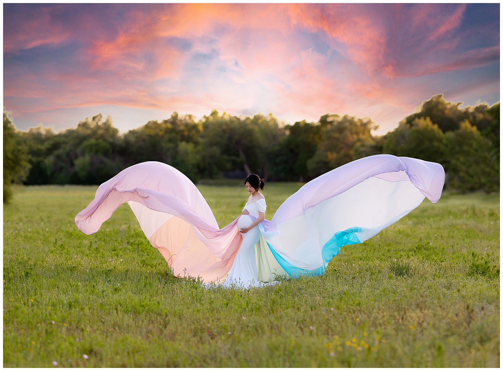 Woman in a rainbow maternity gown standing in a field of wildflowers in front of a sunset