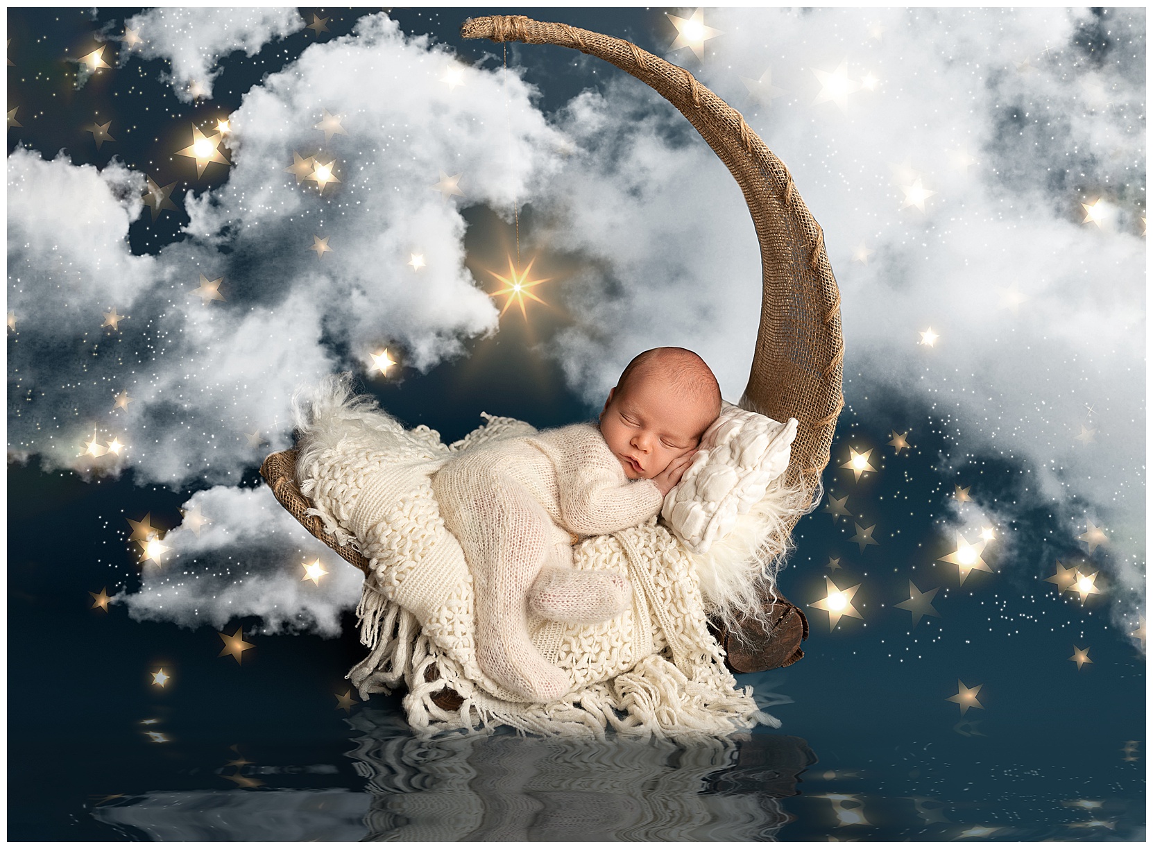 Sleepy newborn baby on a jute moon prop in front of a background of stars and clouds. Baby is swaddled in a white knit jumper and propped on a white blanket and pillow.