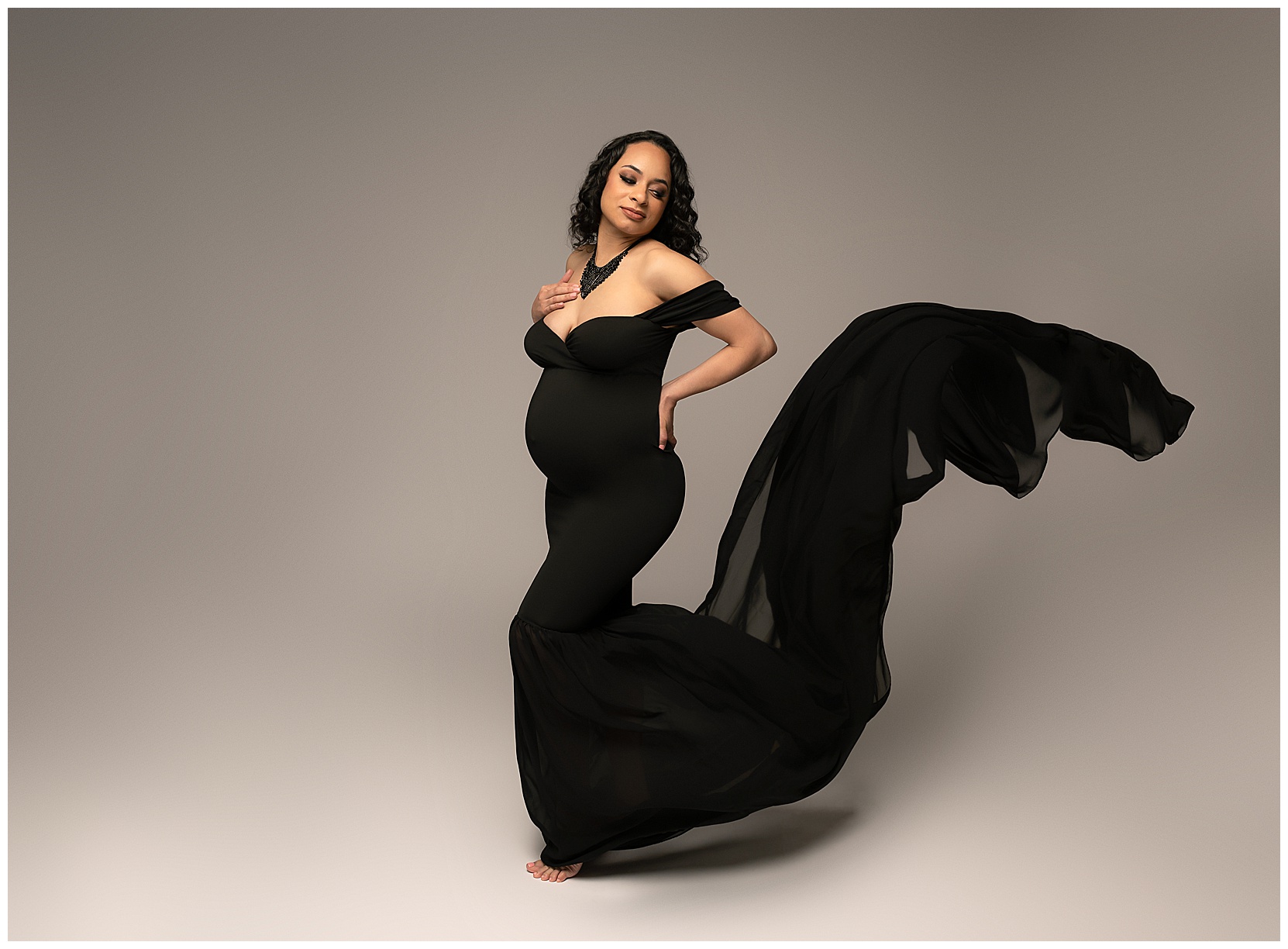 Pic 3: A dramatic color baby bump photo of a pregnant woman in a black maternity gown in front of a plain gray background.
