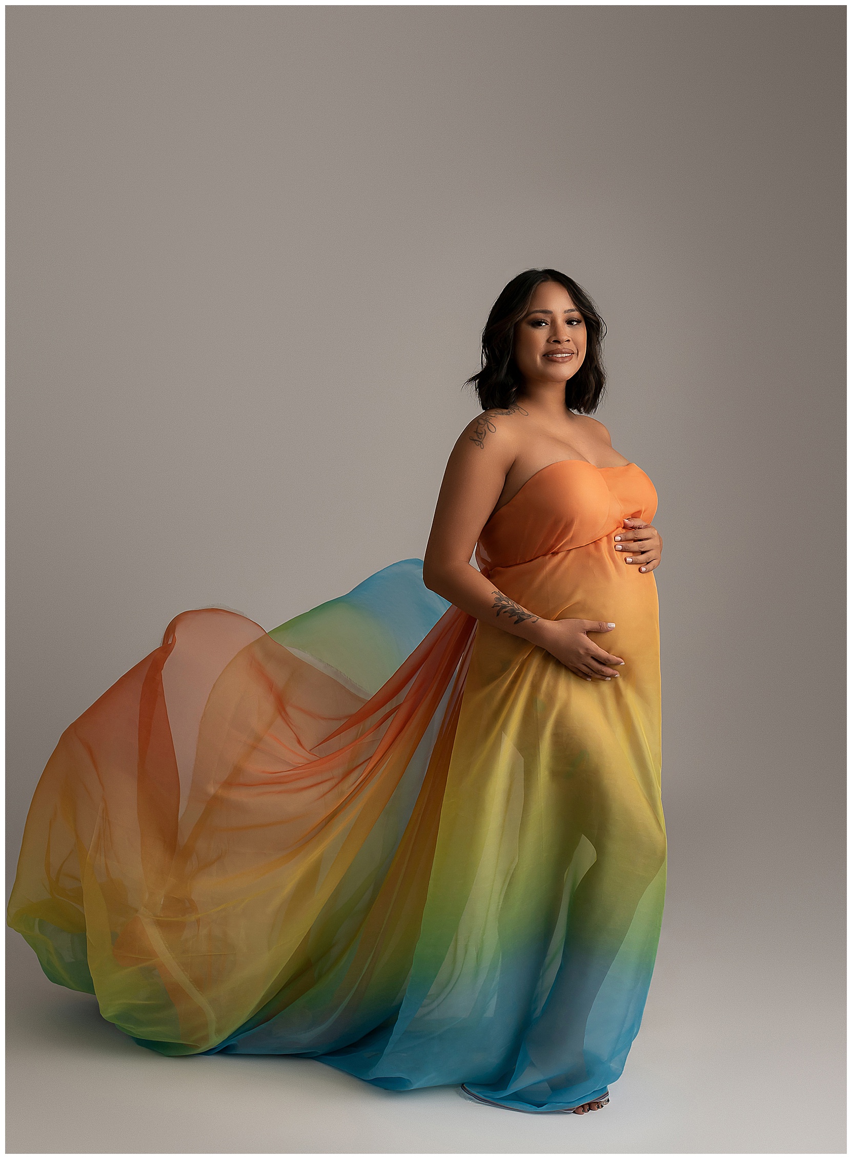 Studio maternity photo featuring a woman in a rainbow gown