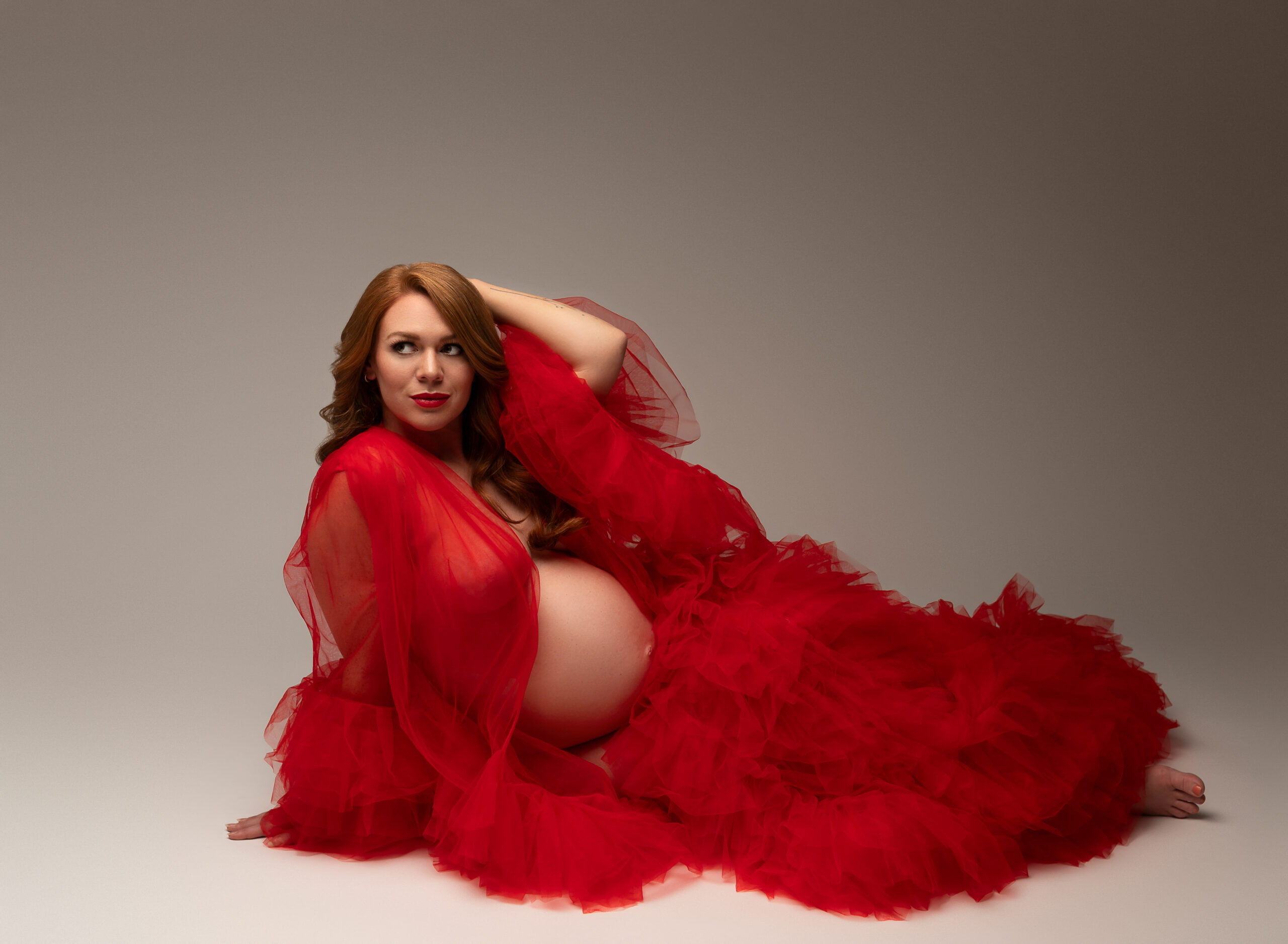 Woman on a neutral black and white background wearing a red taffeta maternity dress. 