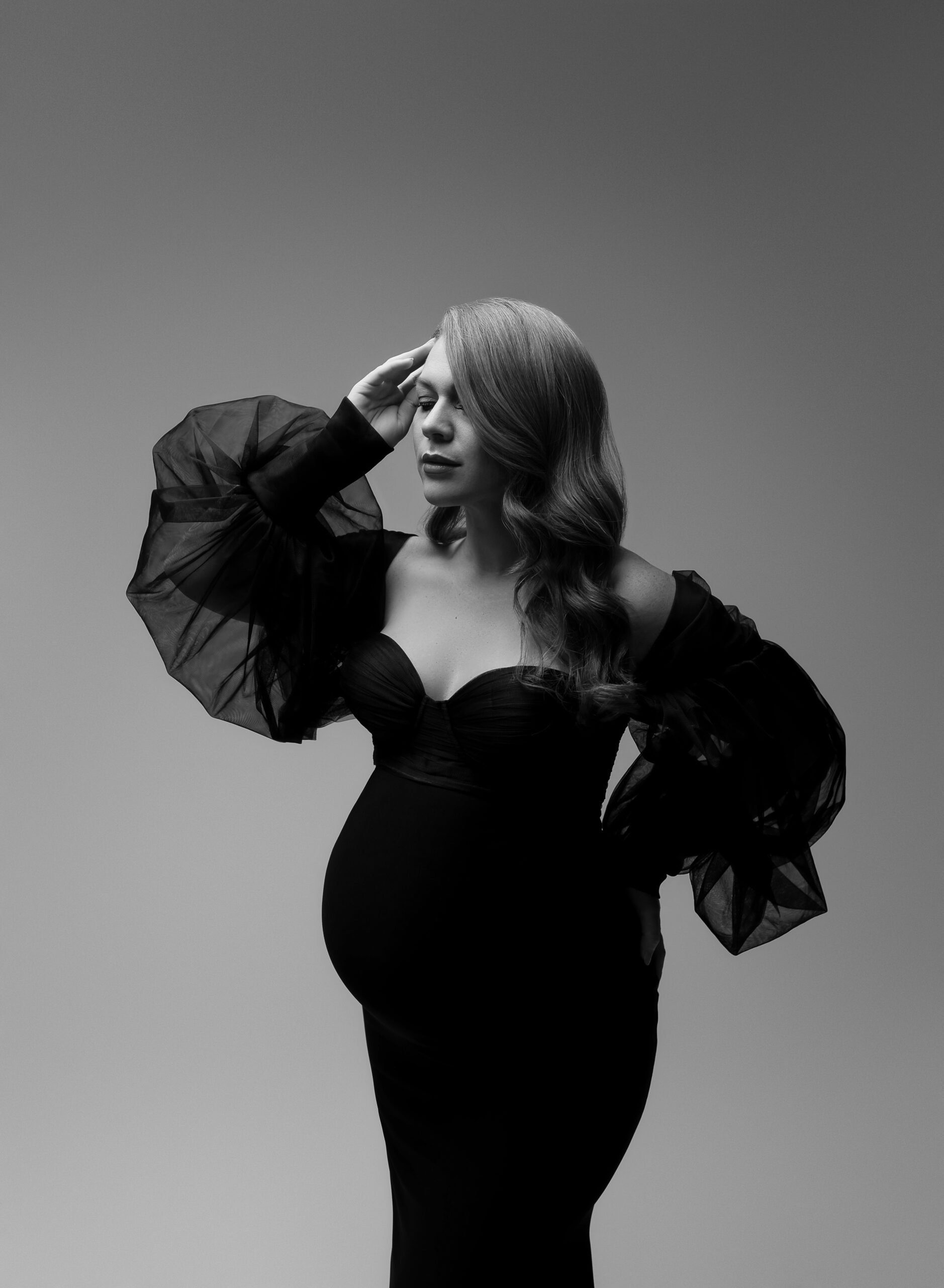 A close-up black and white maternity photo featuring a woman in a black maternity gown with puff sleeves.