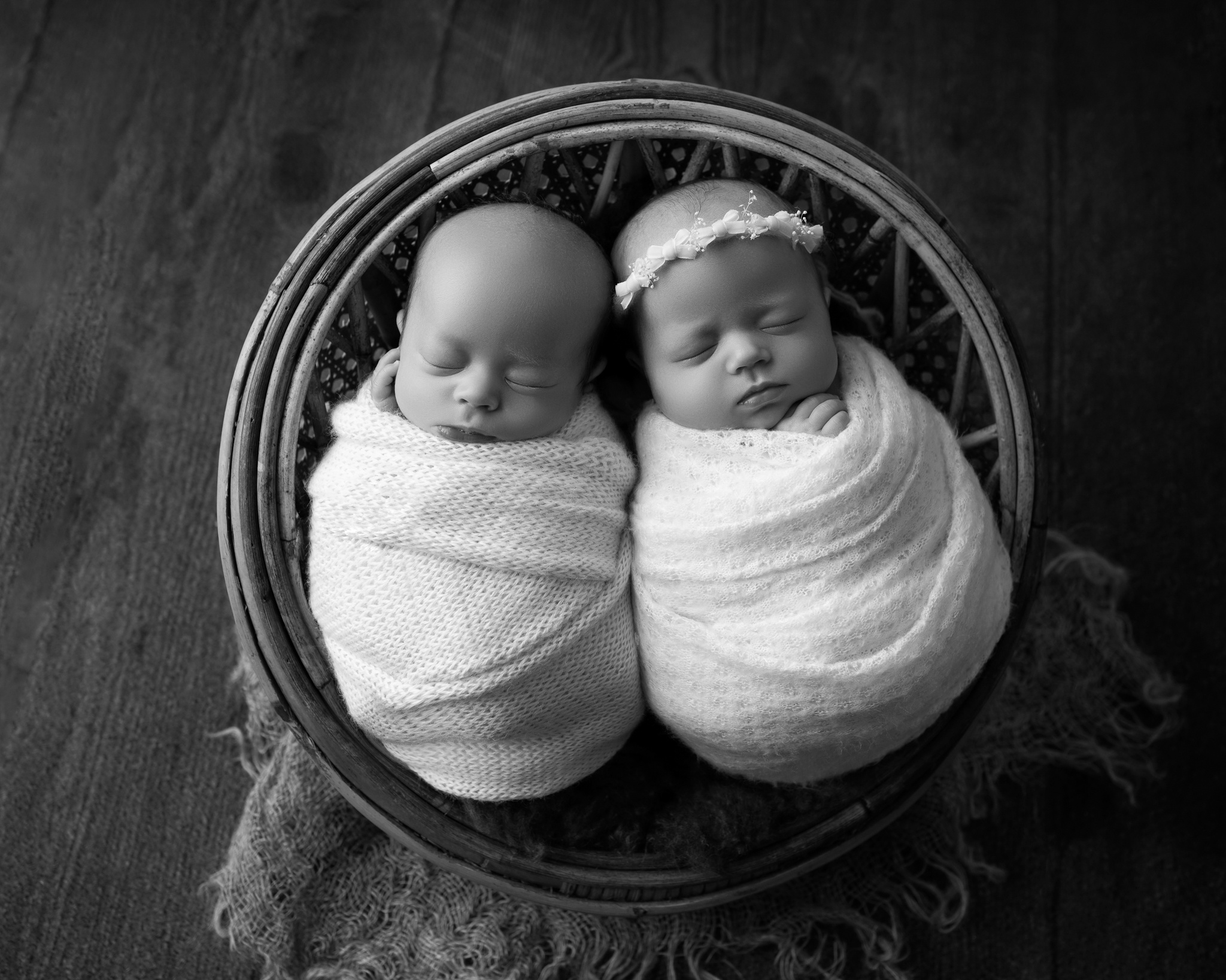 a black and white newborn twin photo featuring two newborn babies swaddled in white and posed in a basket.