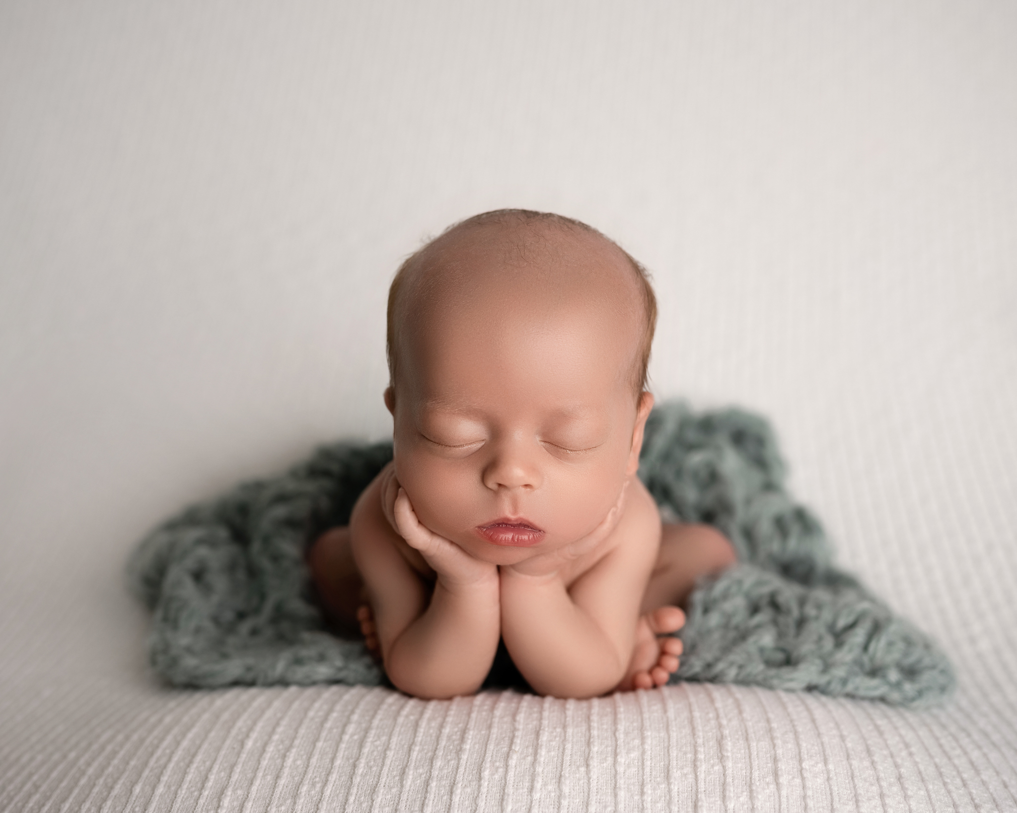 Twin newborn photo featuring one of the two posed in froggy pose on a fluffy, blue blanket in front of a white background. 