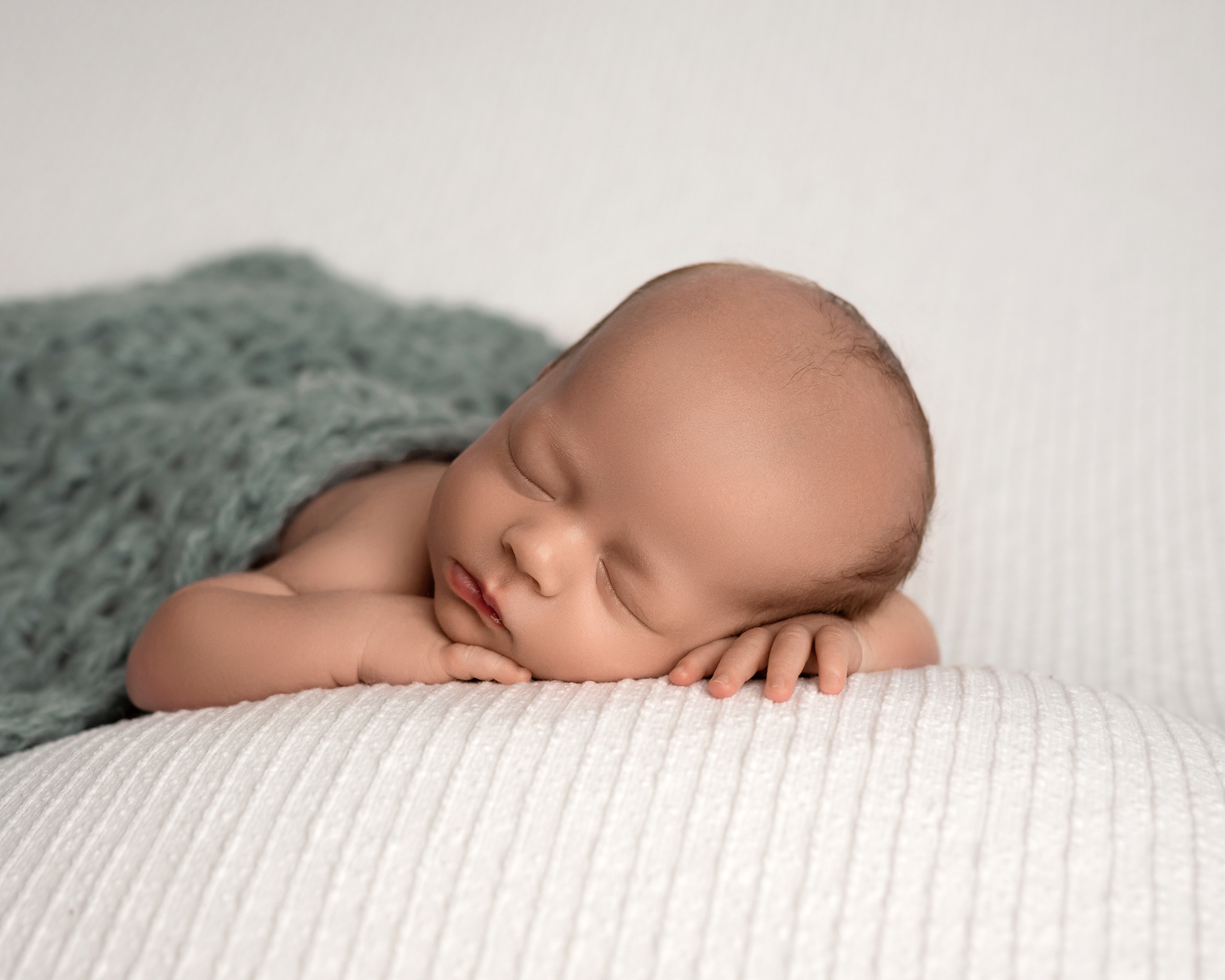 Newborn photo featuring a sleeping baby boy posed on a white background. 