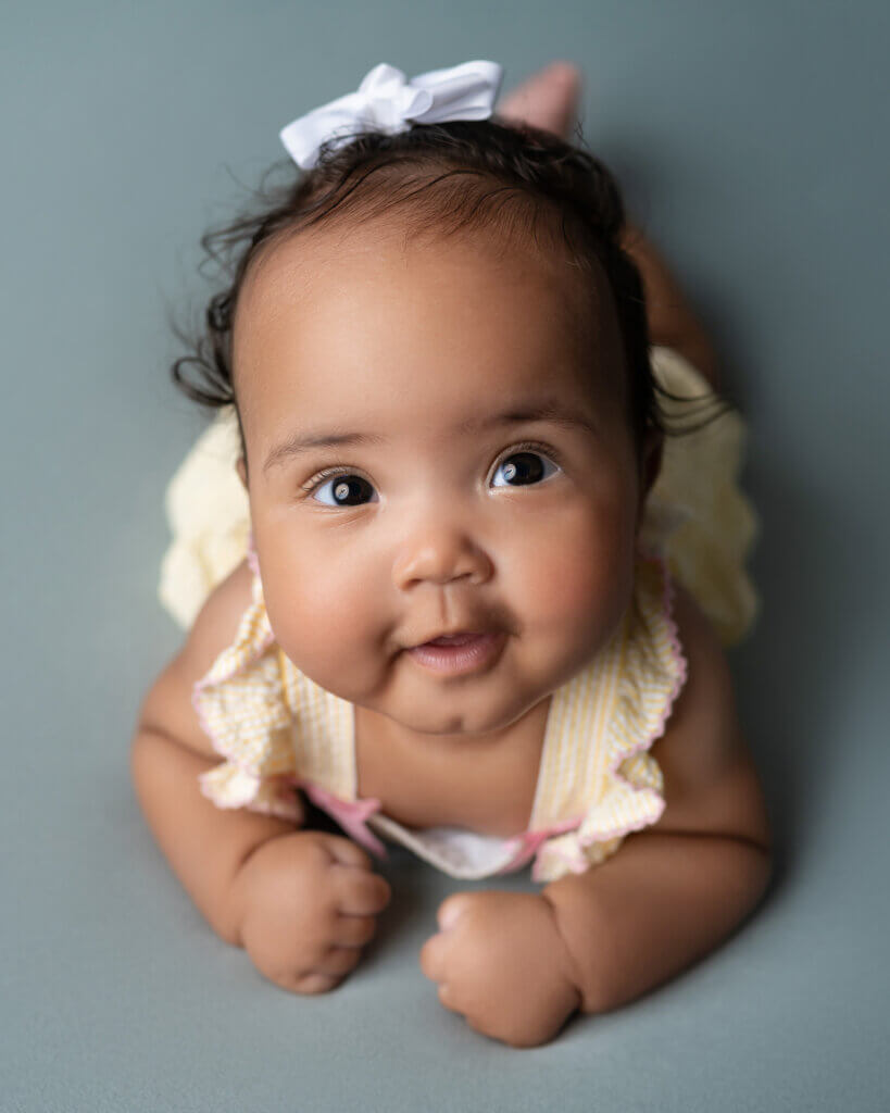 baby girl tummy time yellow outfit smiling and looking at camera