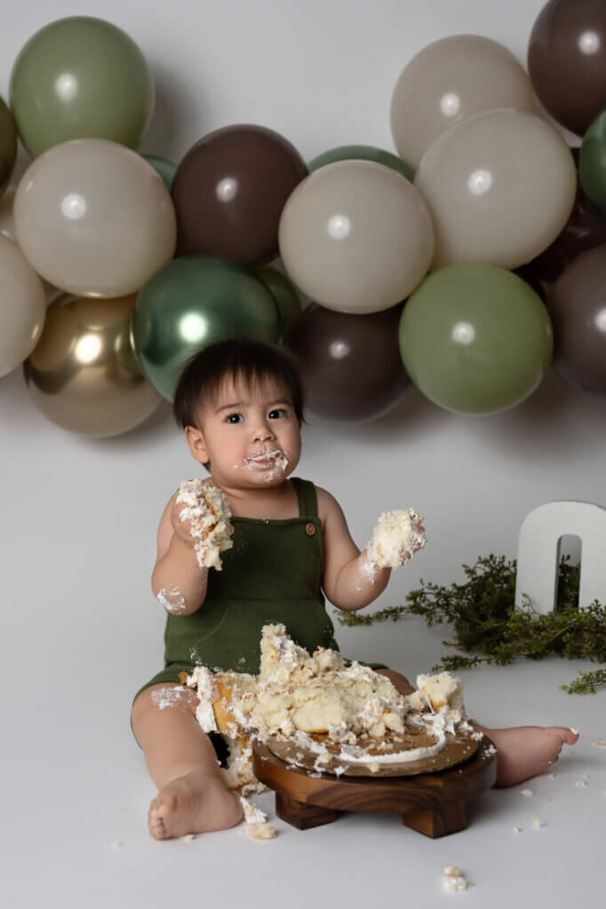 baby wearing green romper with funny face during cakesmash photoshoot in austin.