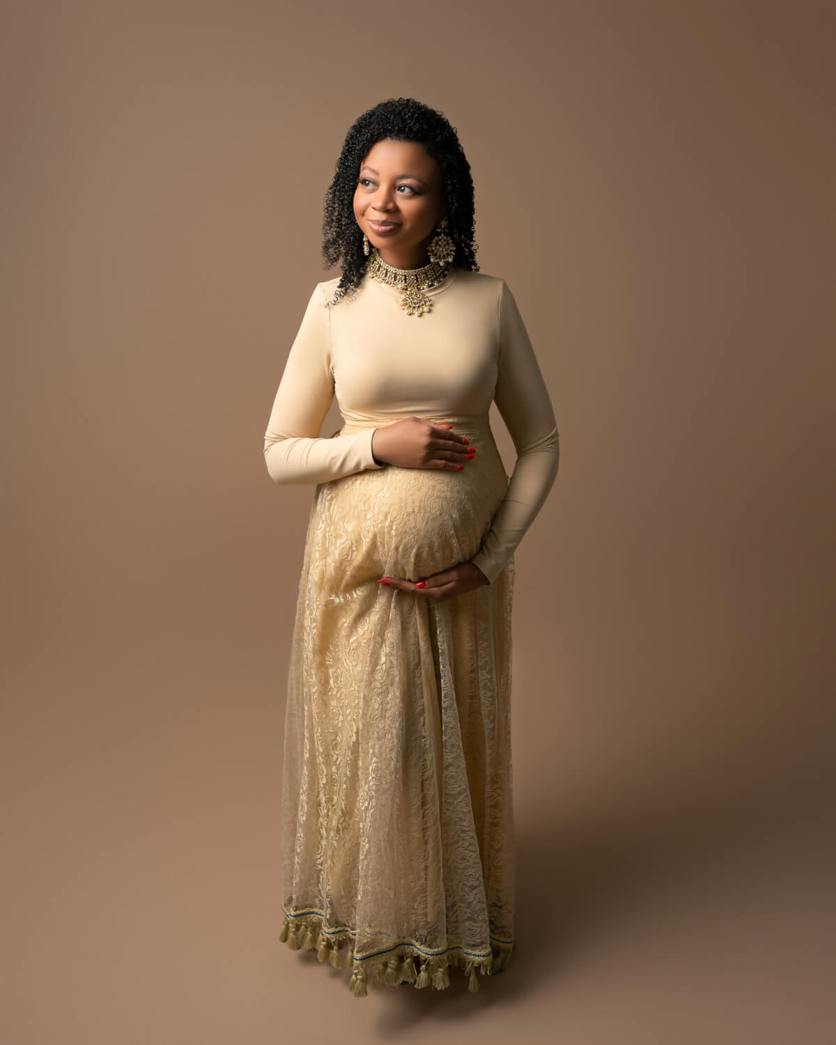A color maternity portrait of a woman in traditional gold clothing holding her pregnant belly. 