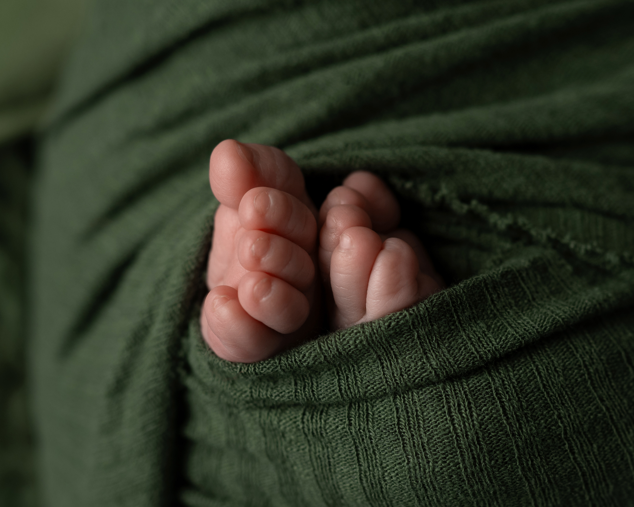 A close-up of a newborn's feet swaddled in green fabric.