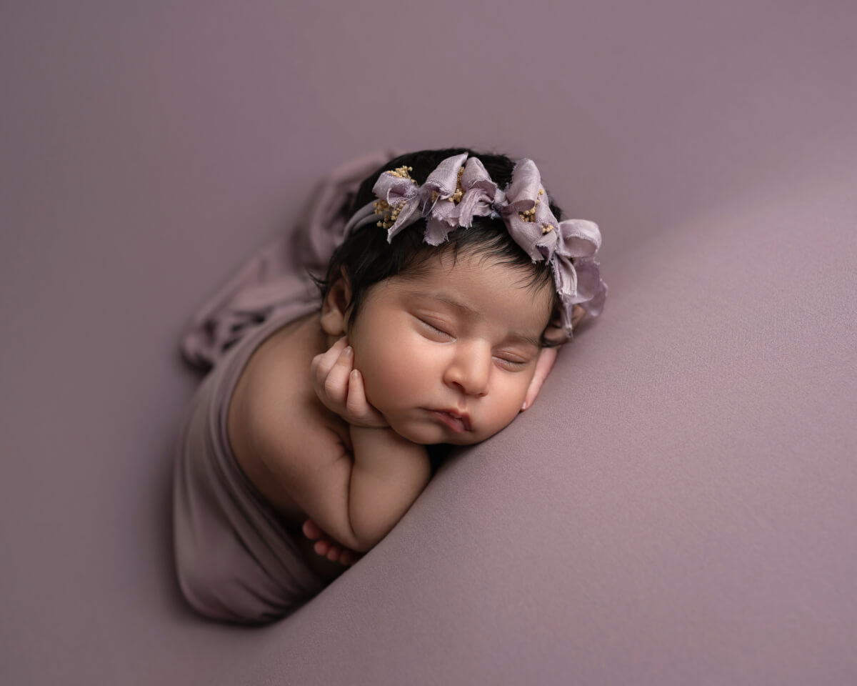 Newborn baby girl in mauve wrap with floral headband posed on seamless backdrop | Austin newborn photographer serving Westlake and Leander