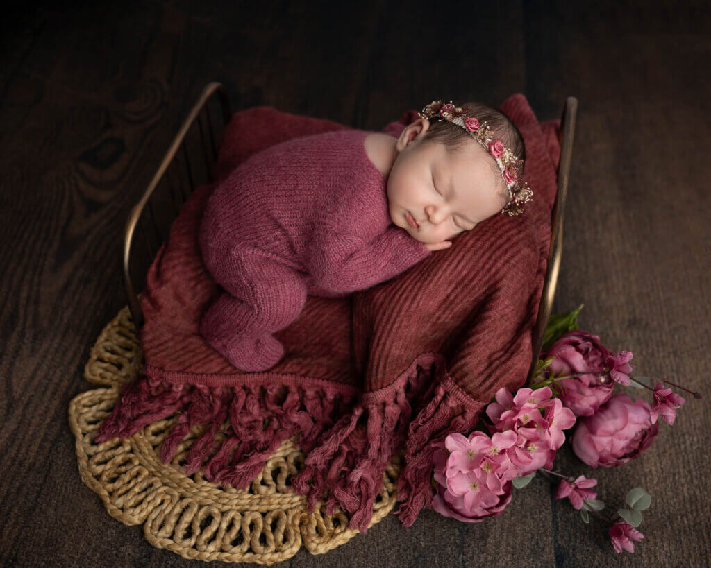 baby girl in mauve knit outfit sleeping on tiny bed with pink flowers