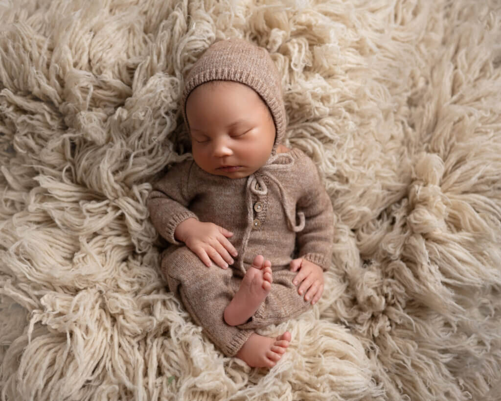 newborn boy in brown knit romper laying on beige carpet